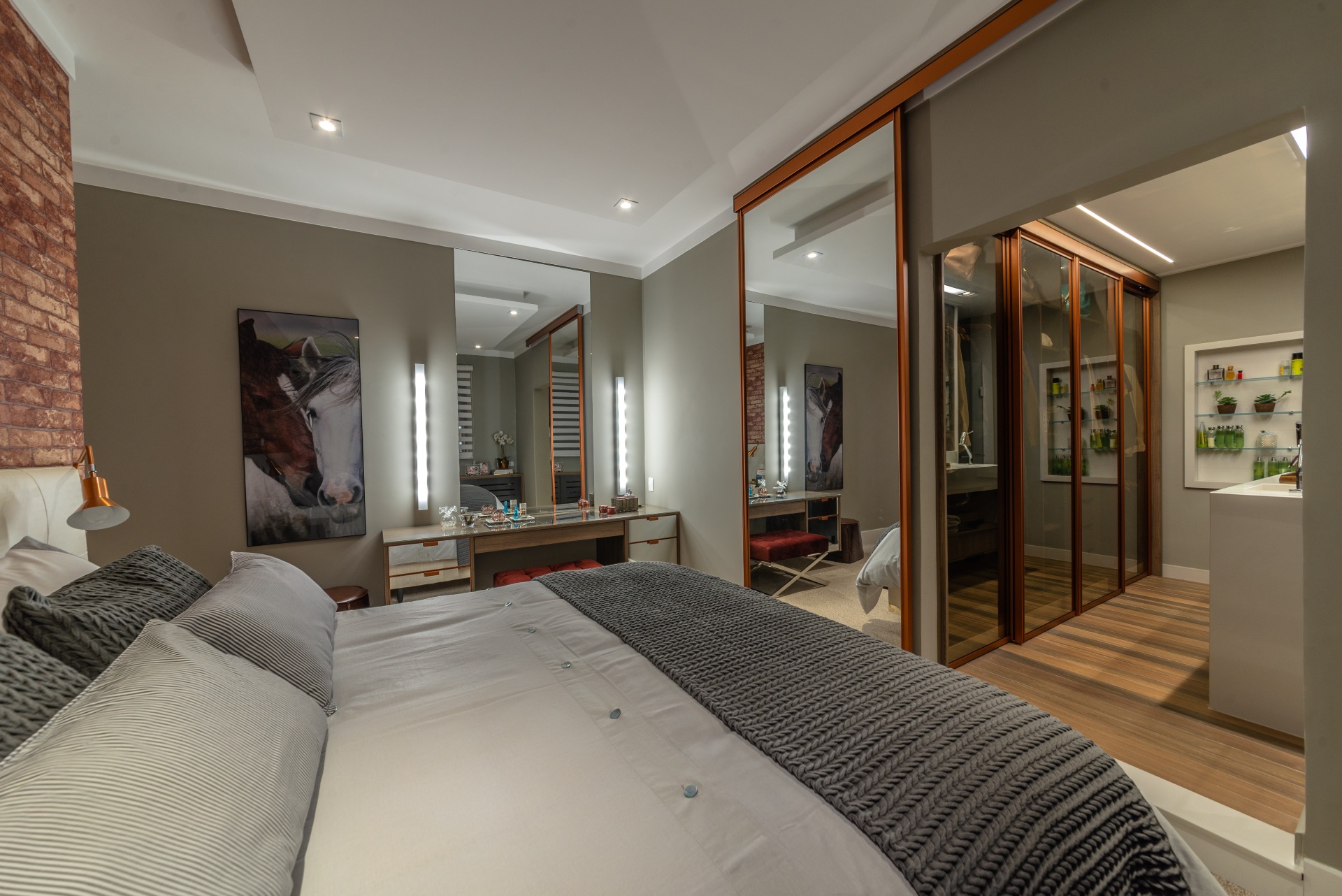 Ambiente elegante, com cama grande, tons acinzentados e iluminação suave. Destaque para texturas aconchegantes e marcenaria planejada