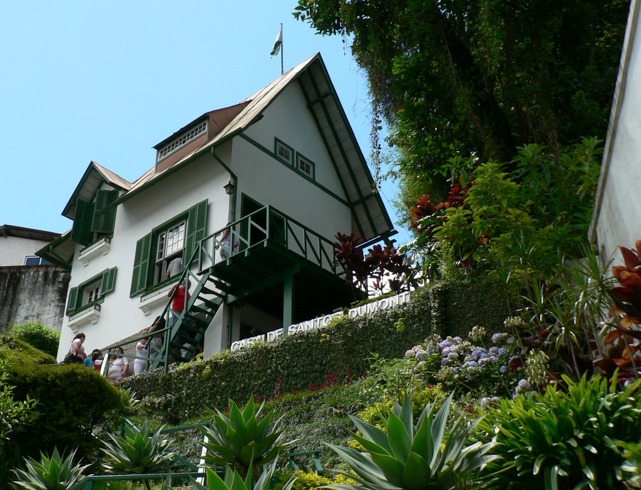 Casa pitoresca, de três andares, com paredes brancas e detalhes verdes construída sobre jardim íngreme