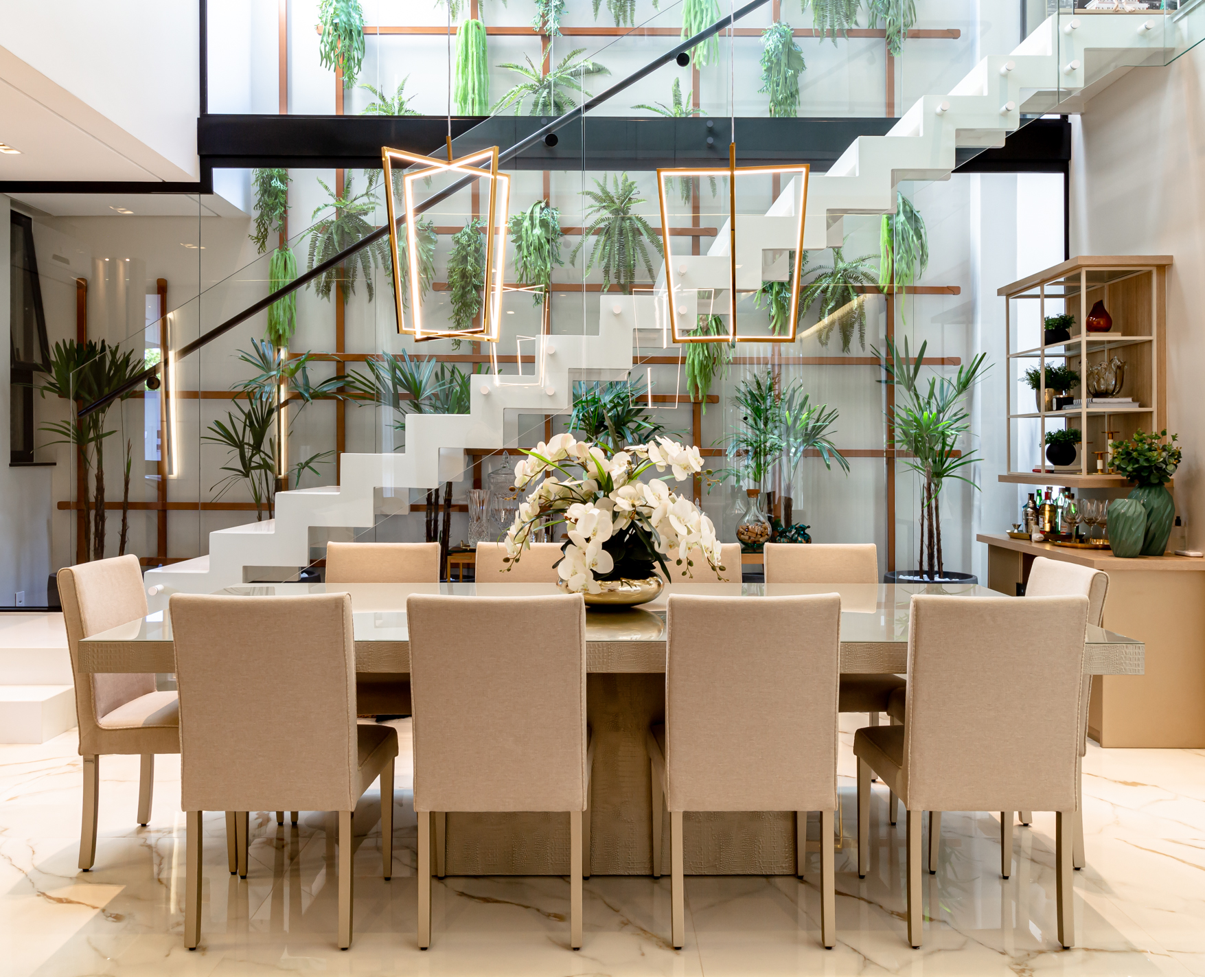orquídeia Ambiente de jantar contemporâneo com mesa retangular, oito cadeiras estofadas e arranjo central de orquídeas brancas, integrado a um espaço com escada branca flutuante e jardim vertical ao fundo.