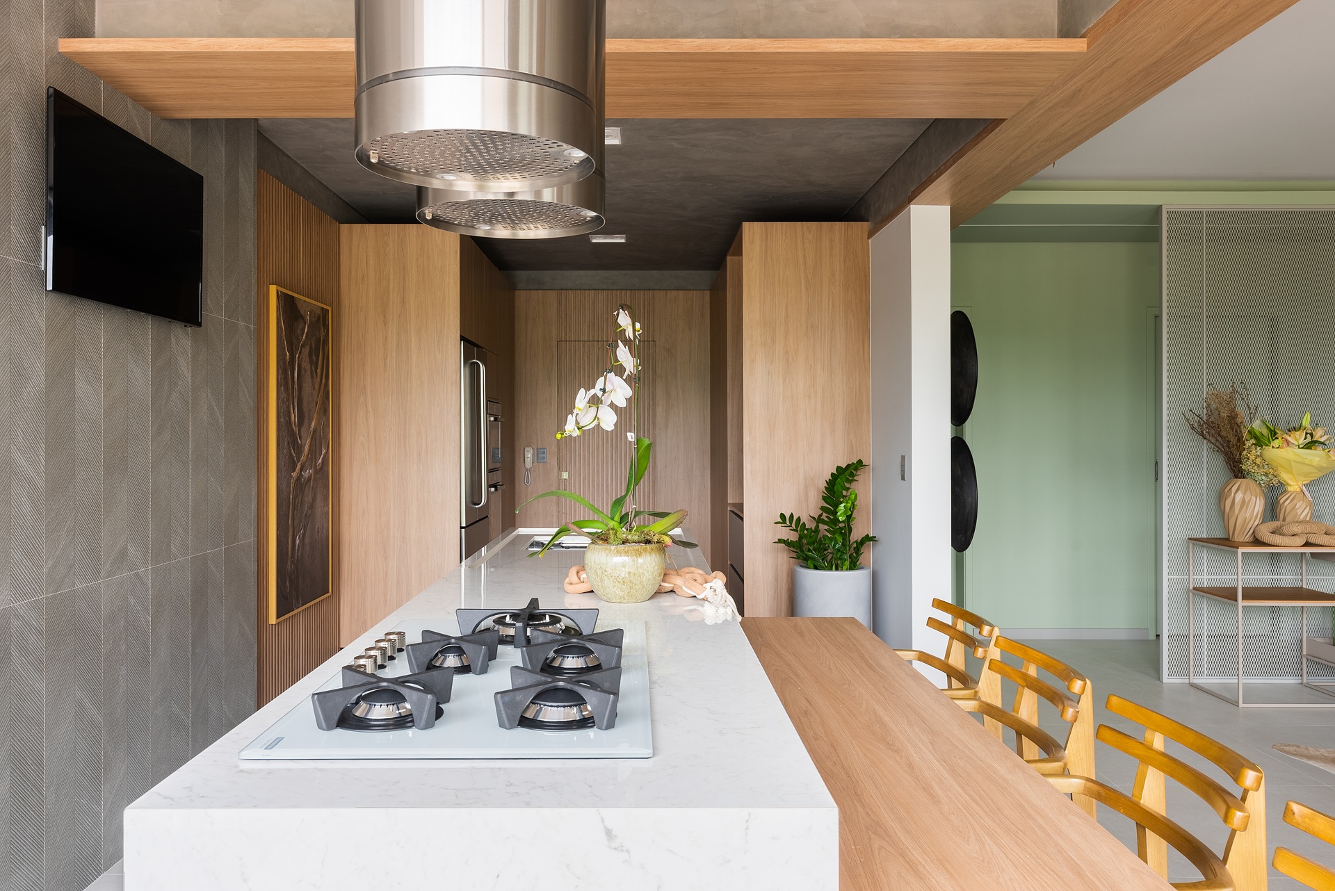 orquídea Cozinha contemporânea com ilha central em mármore claro, cooktop embutido e vaso de orquídea branca ao centro, em ambiente bem iluminado e cercado por móveis em madeira clara.