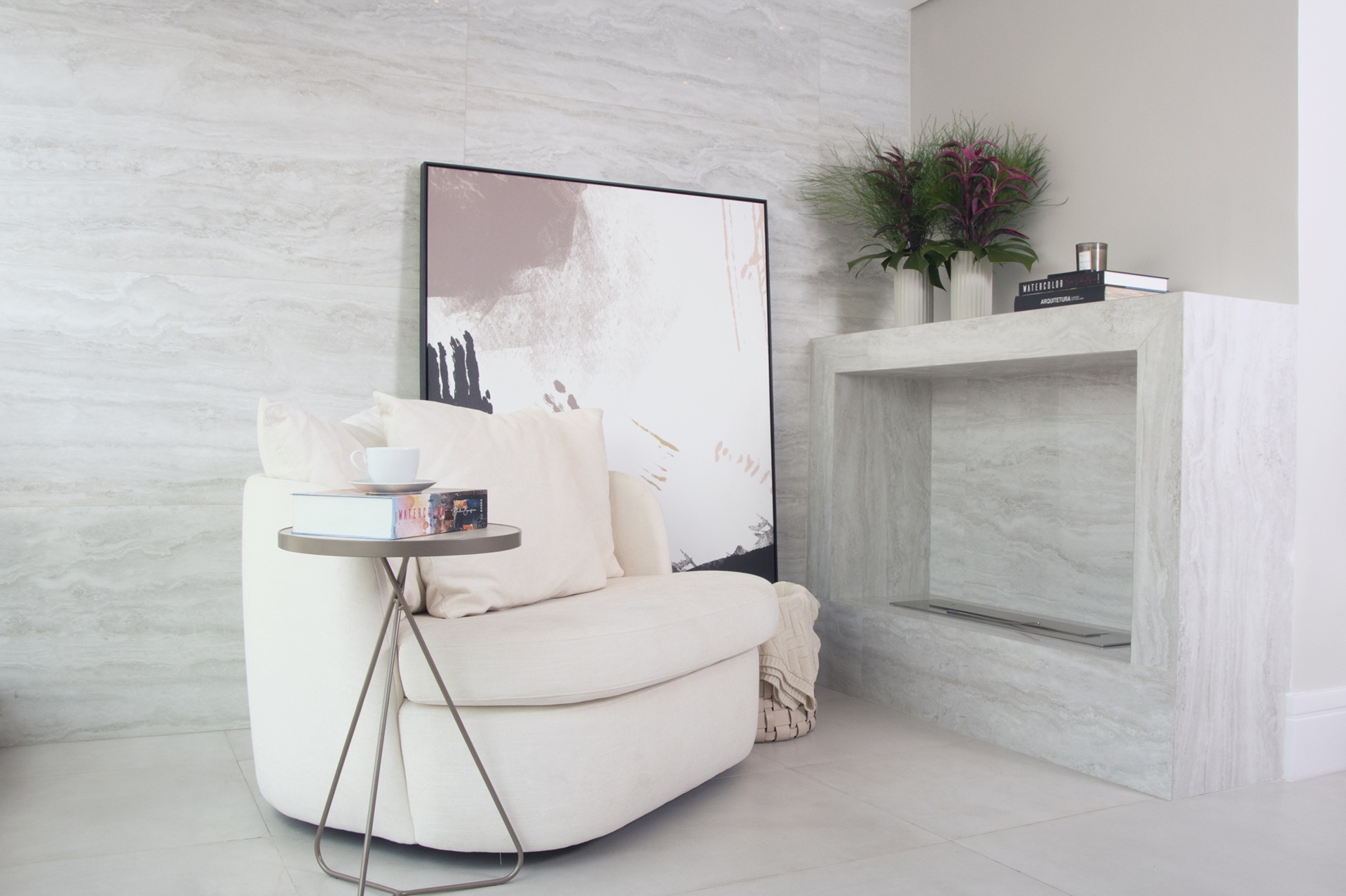 Living com revestimento que reproduz pedra em tom claro, poltrona branca e lareira elétrica