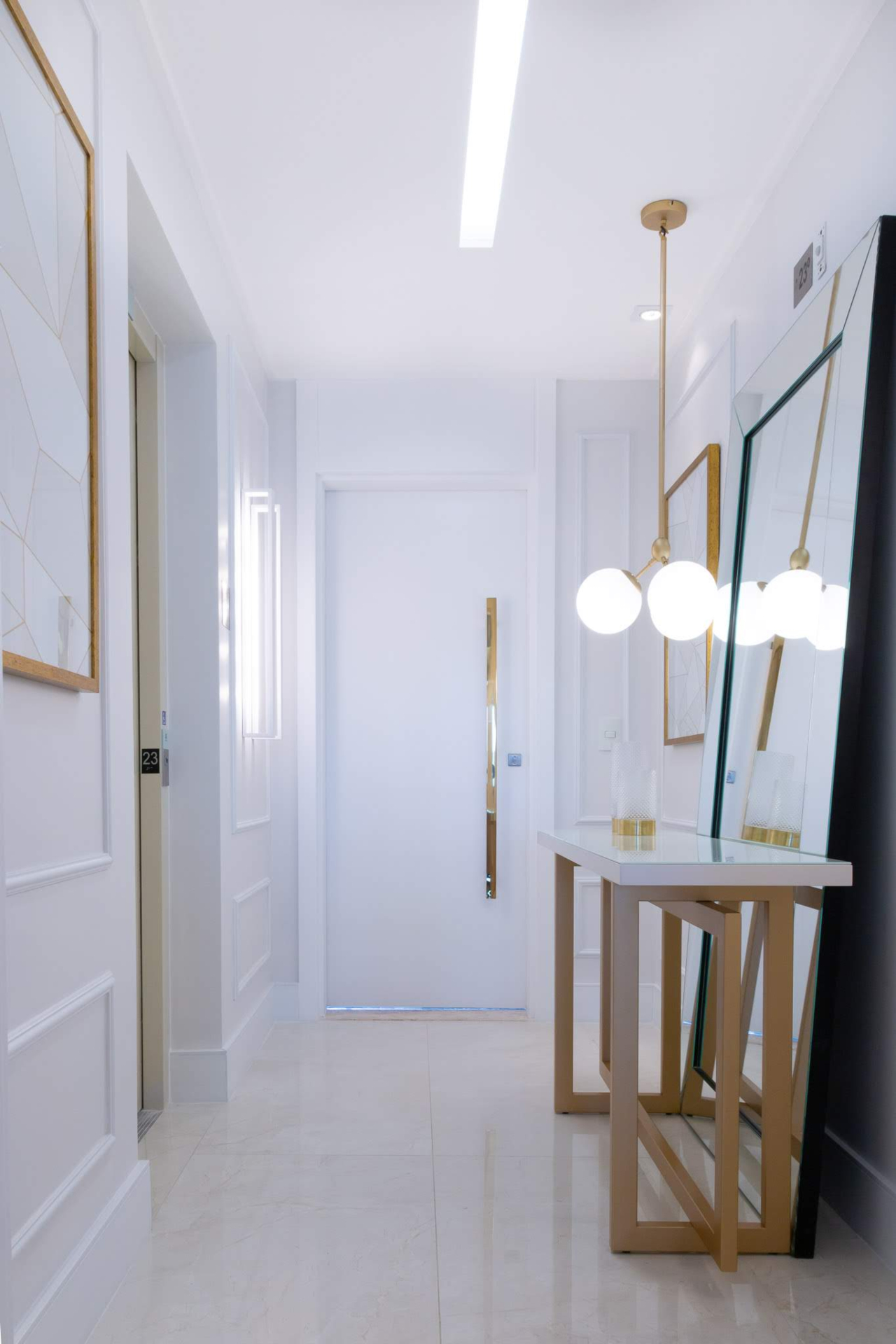 Hall de entrada em branco e dourado com pendentes, espelho e aparador