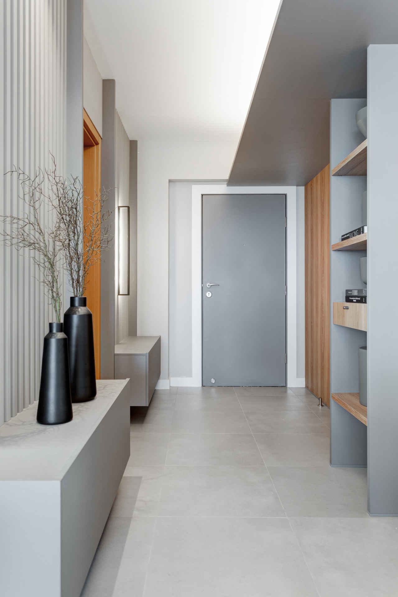 Entrada monocromática e minimalista com iluminação vertical, vasos pretos com plantas e prateleiras de madeira