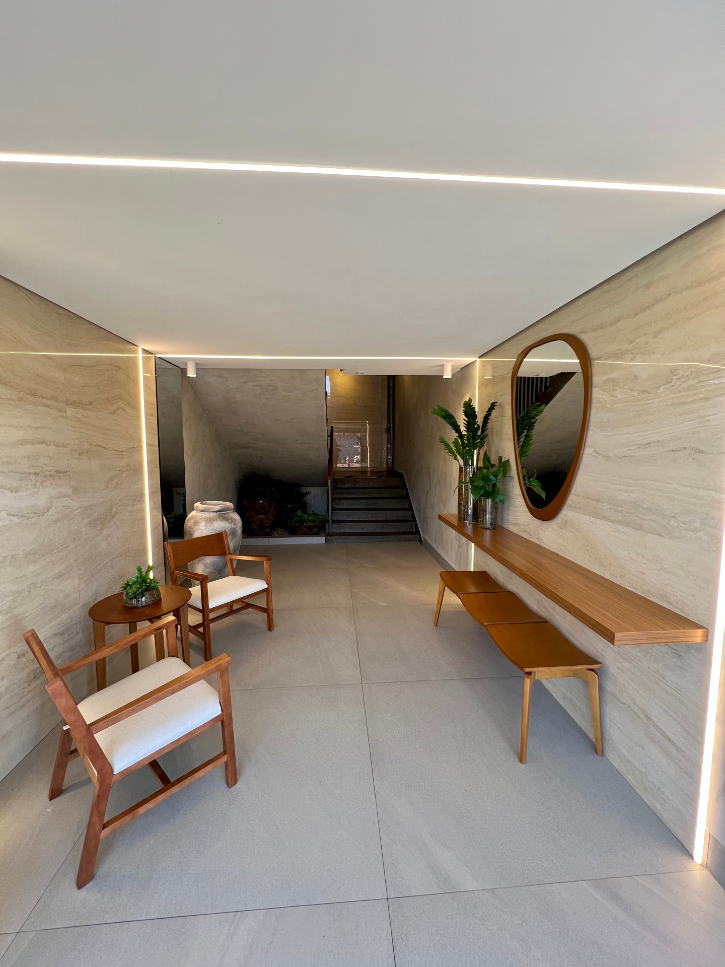 Hall de entrada com cadeiras, bancos e prateleiras de madeira com espelho orgânico na parede