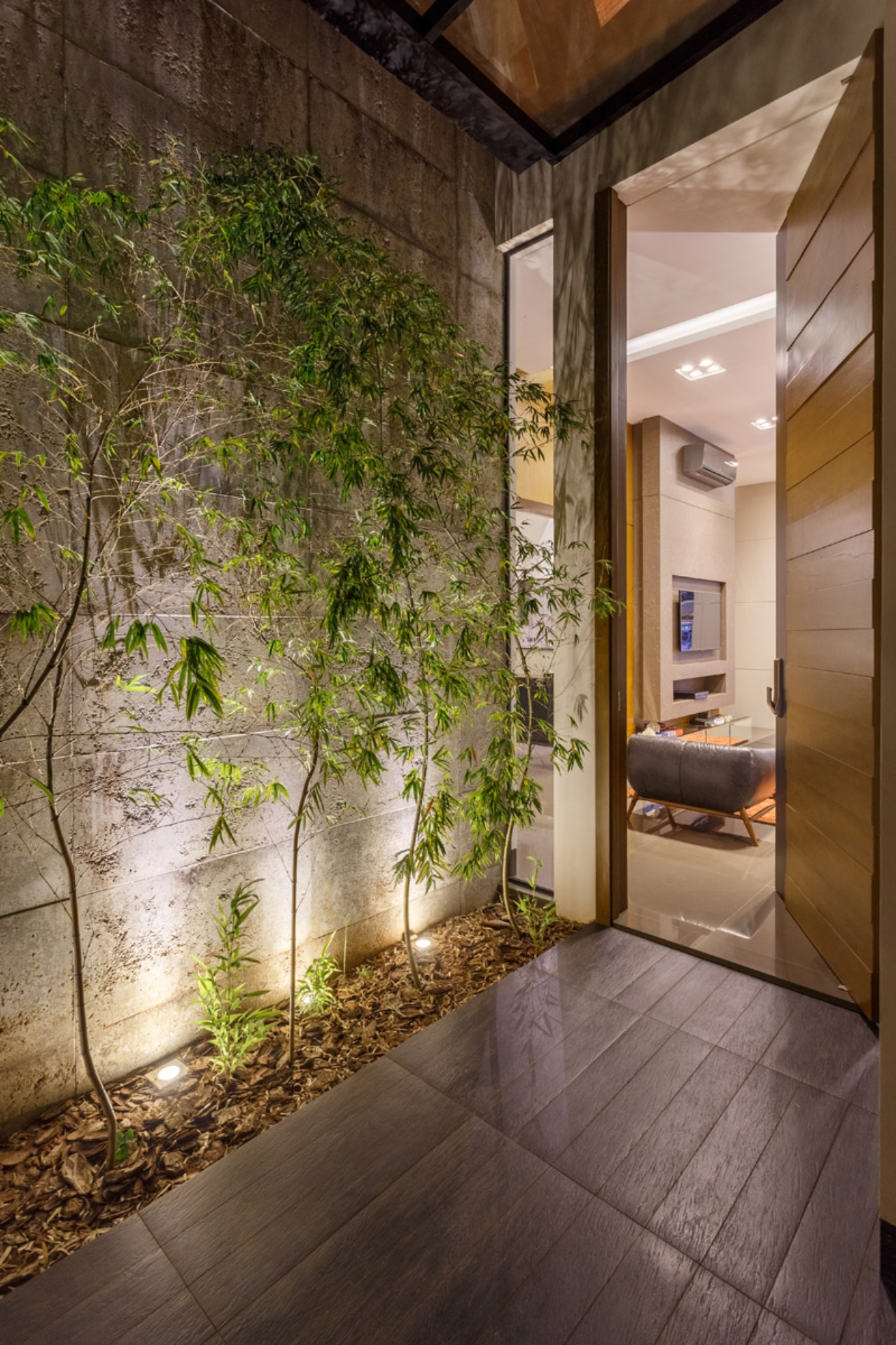 Entrada com jardim interno iluminado e parede de concreto aparente