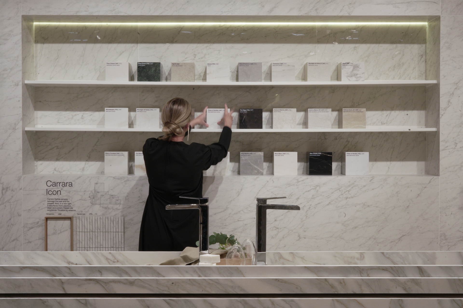 Parede com revestimento Carrara Icon e prateleira com diferentes amostras de porcelanato Portobello sendo organizadas por mulher vestida de preto