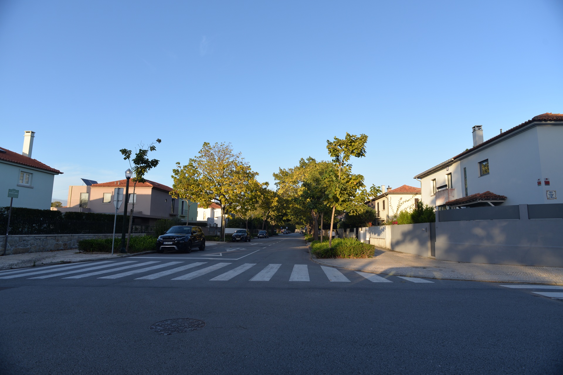 cidades jardim Rua tranquila do Bairro Marechal Gomes da Costa, em Coimbra, Portugal. A imagem mostra casas unifamiliares com jardins, calçadas largas e arborização alinhada, elementos típicos do planejamento inspirado no conceito de cidade-jardim.