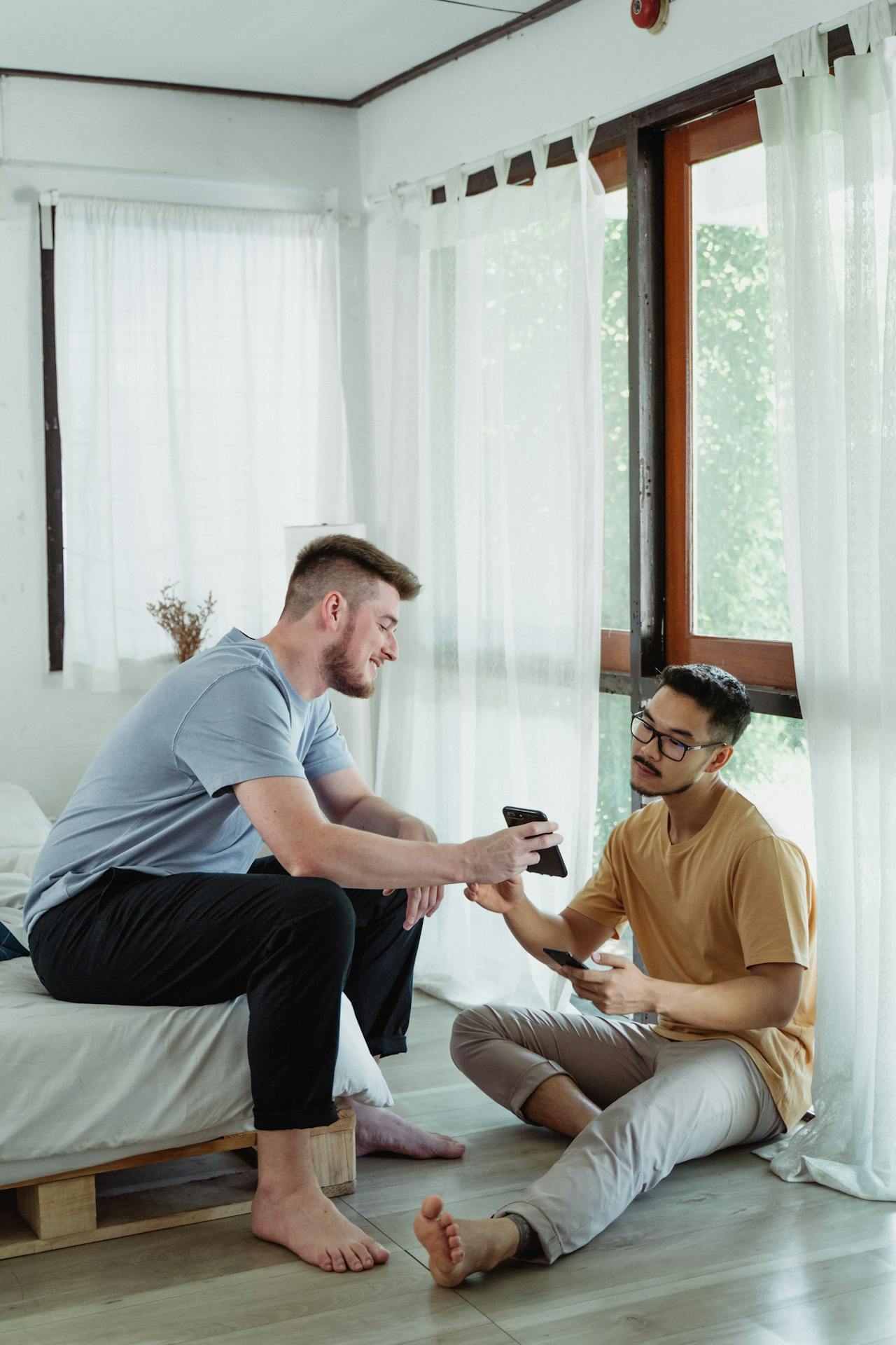 Coliving Dois homens em um ambiente residencial iluminado por luz natural, interagindo de forma descontraída enquanto olham para os seus celulares