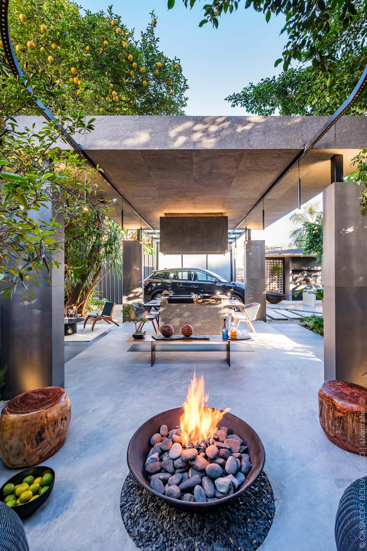 Garagem de estar integrada à natureza, com fire pit, mobiliário moderno, áreas de convívio e o carro compondo a ambientação