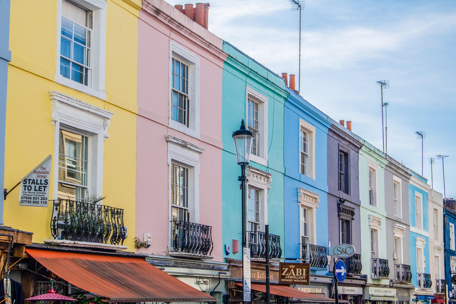 Sequência de casas geminadas com fachadas coloridas no estilo vitoriano, típicas de Portobello Road. As varandas de ferro trabalhado e as janelas simétricas compõem a paisagem urbana do bairro