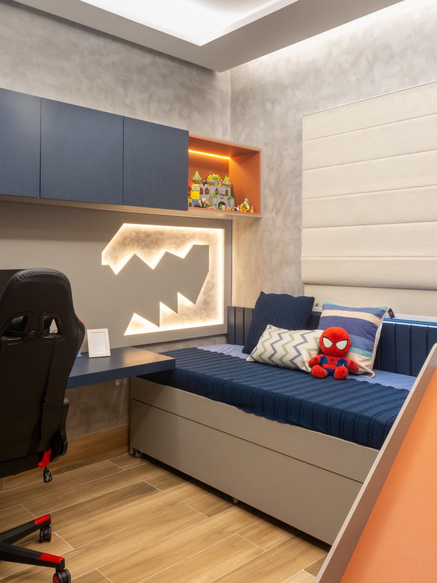 Quarto em tons de azul e laranja. Há uma cama com escrivaninha e armário suspenso na parede