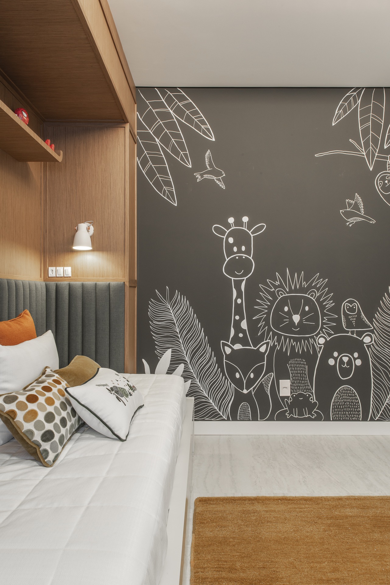 Quarto de pré-adolescente. À esquerda está a cama. Ao fundo tem uma parede revestida de tinta de lousa com bichos