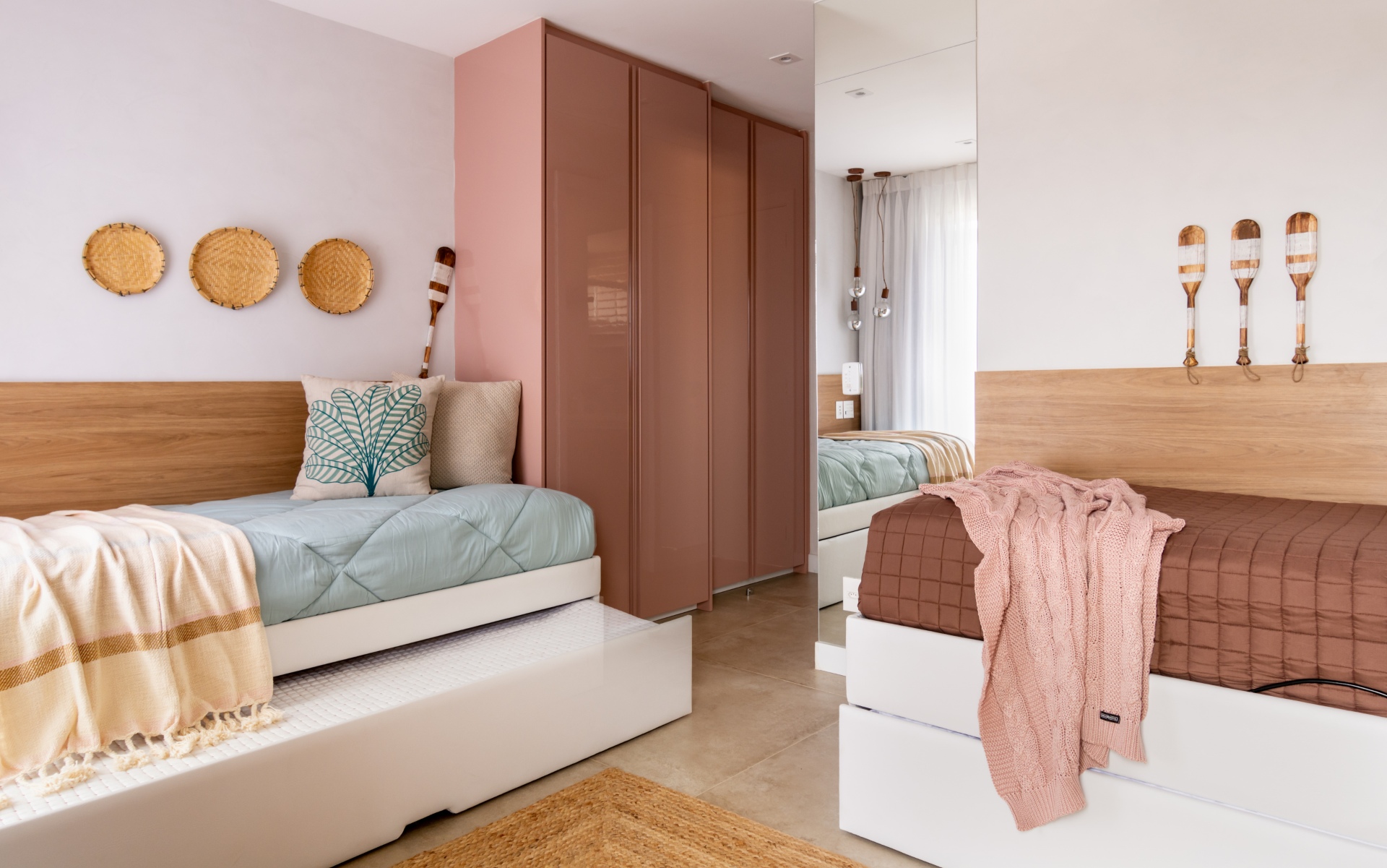 Quarto juvenil em tons de rosa, branco e menta. Há duas camas em primeiro plano e um guarda-roupa cor de rosa ao fundo