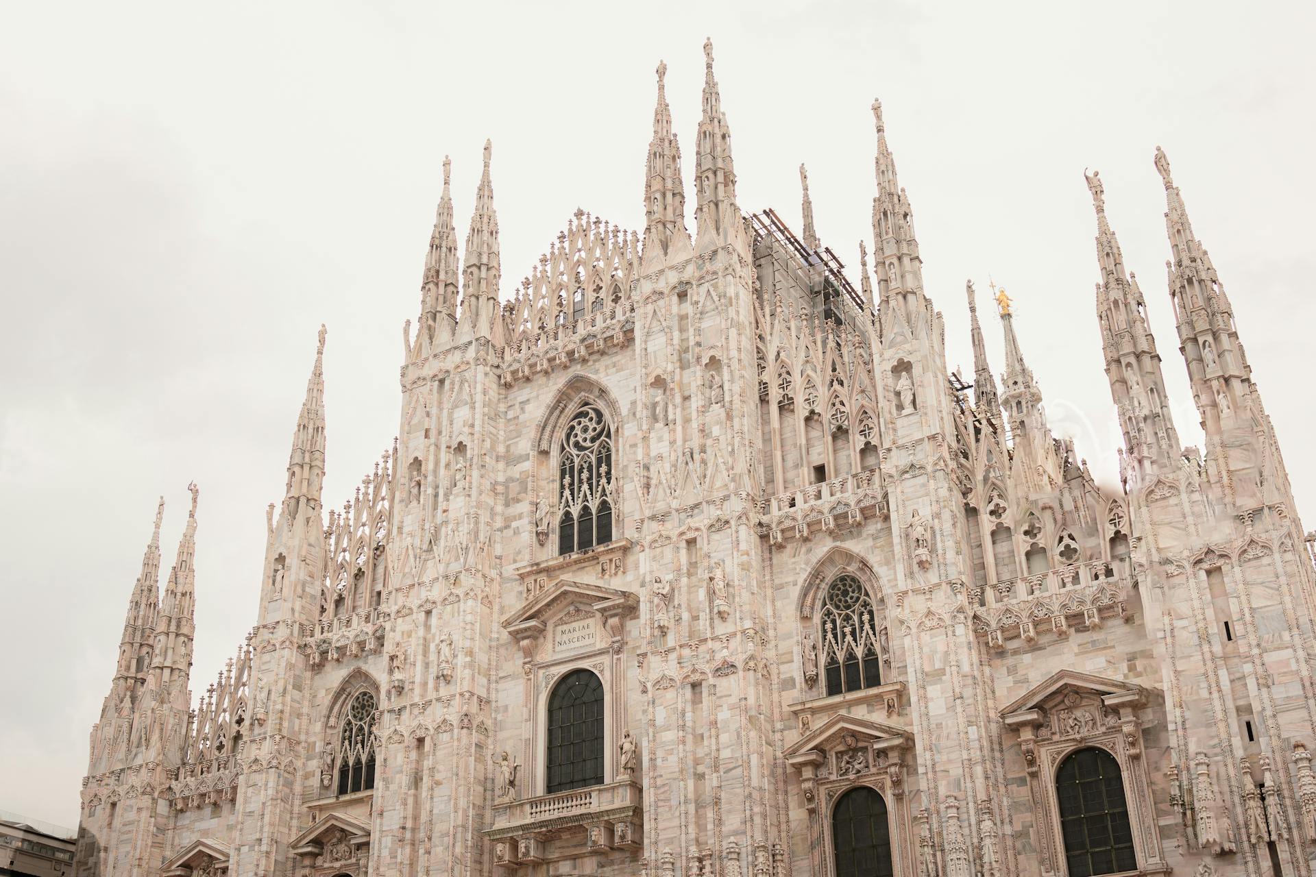 Fachada detalhada do Duomo de Milão, com torres pontiagudas, vitrais e esculturas ornamentadas, representando a grandiosidade da arquitetura gótica