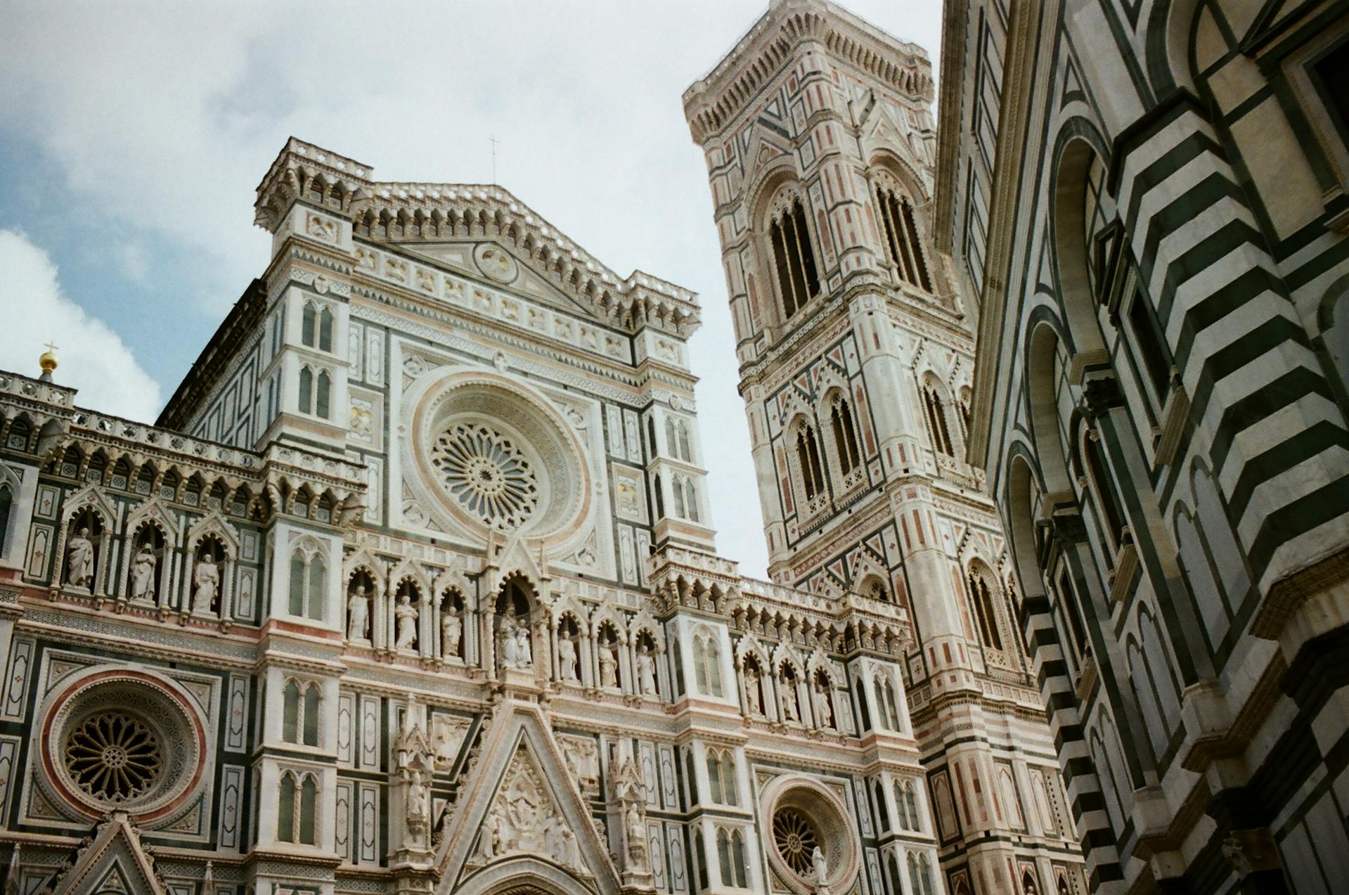 Detalhe da fachada da Basílica de Santa Maria Novella, em Florença, Itália, com esculturas, vitrais e padrões geométricos em mármore colorido, representando o estilo ornamentado do período gótico-renascentista