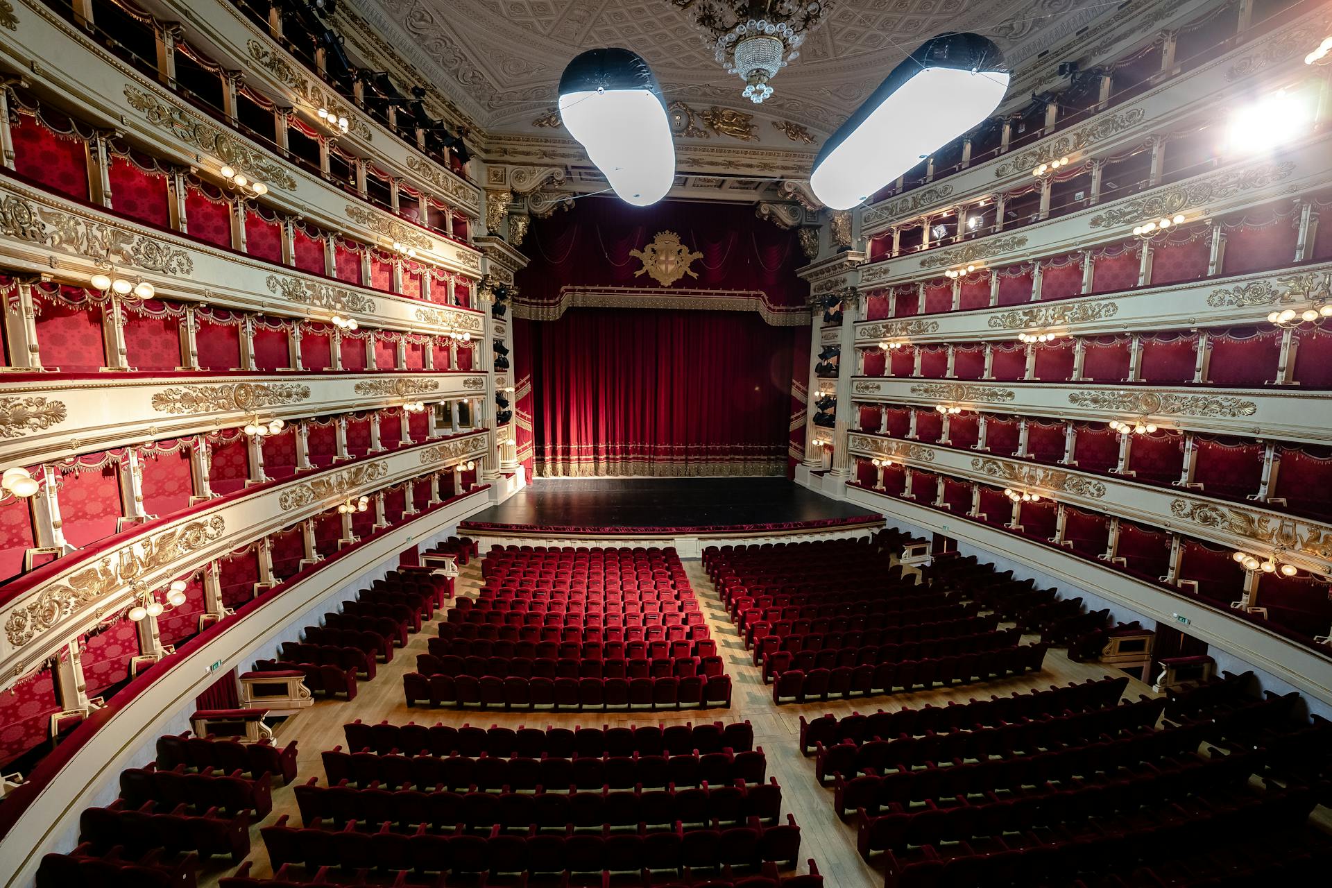 Interior do Teatro alla Scala, em Milão, com assentos vermelhos, varandas luxuosas decoradas com dourado e cortina de veludo no palco, refletindo elegância e grandiosidade