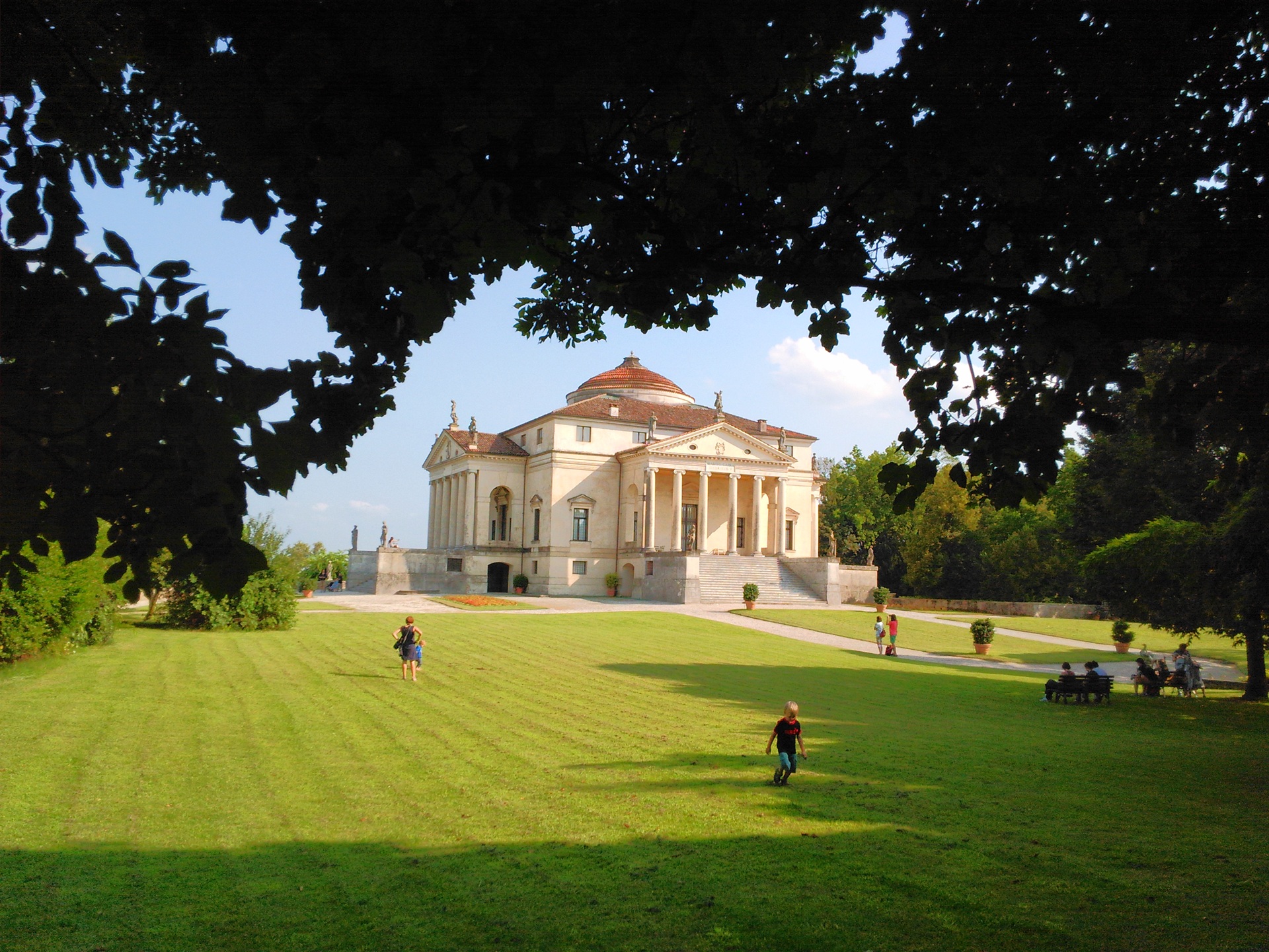 Vista frontal da Villa Rotonda, em Vicenza, Itália, cercada por gramado verde e árvores. O edifício apresenta cúpula central e fachadas idênticas com colunas clássicas, refletindo equilíbrio e harmonia arquitetônica