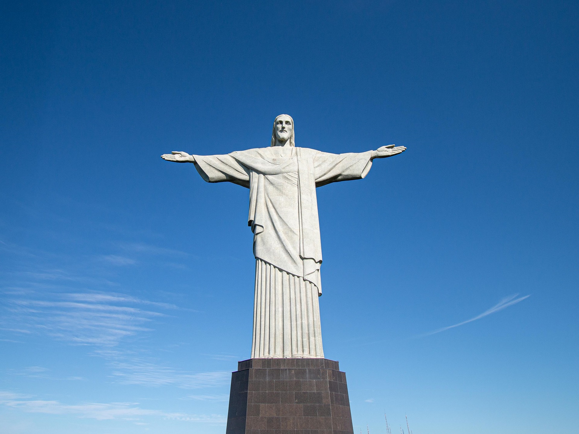 Escultura monumental do Cristo Redentor, de braços abertos sobre o pedestal no topo do Corcovado, sob o céu limpo de um azul intenso