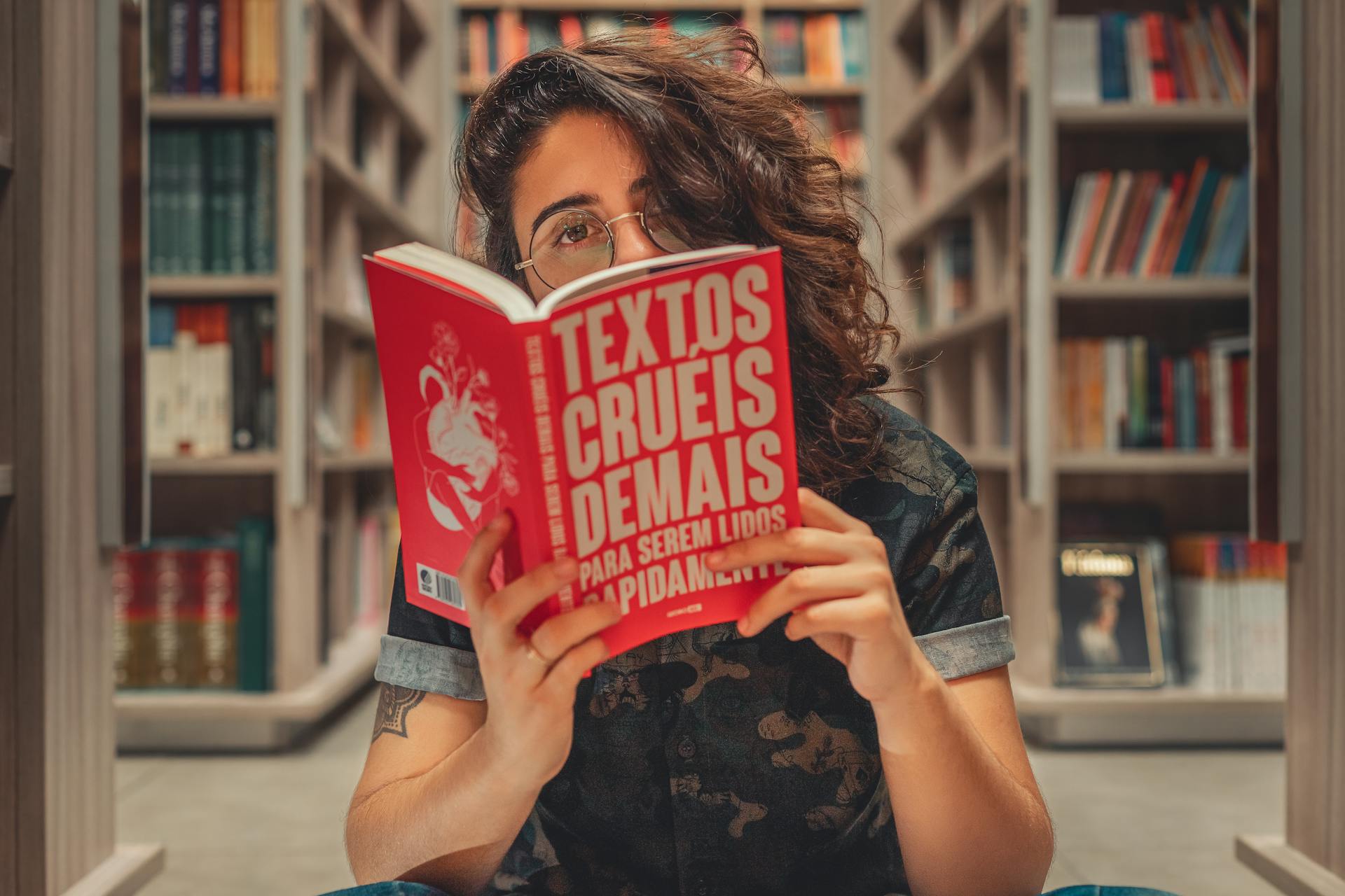 Mulher lendo livro em biblioteca. O livro cobre boa parte de seu rosto