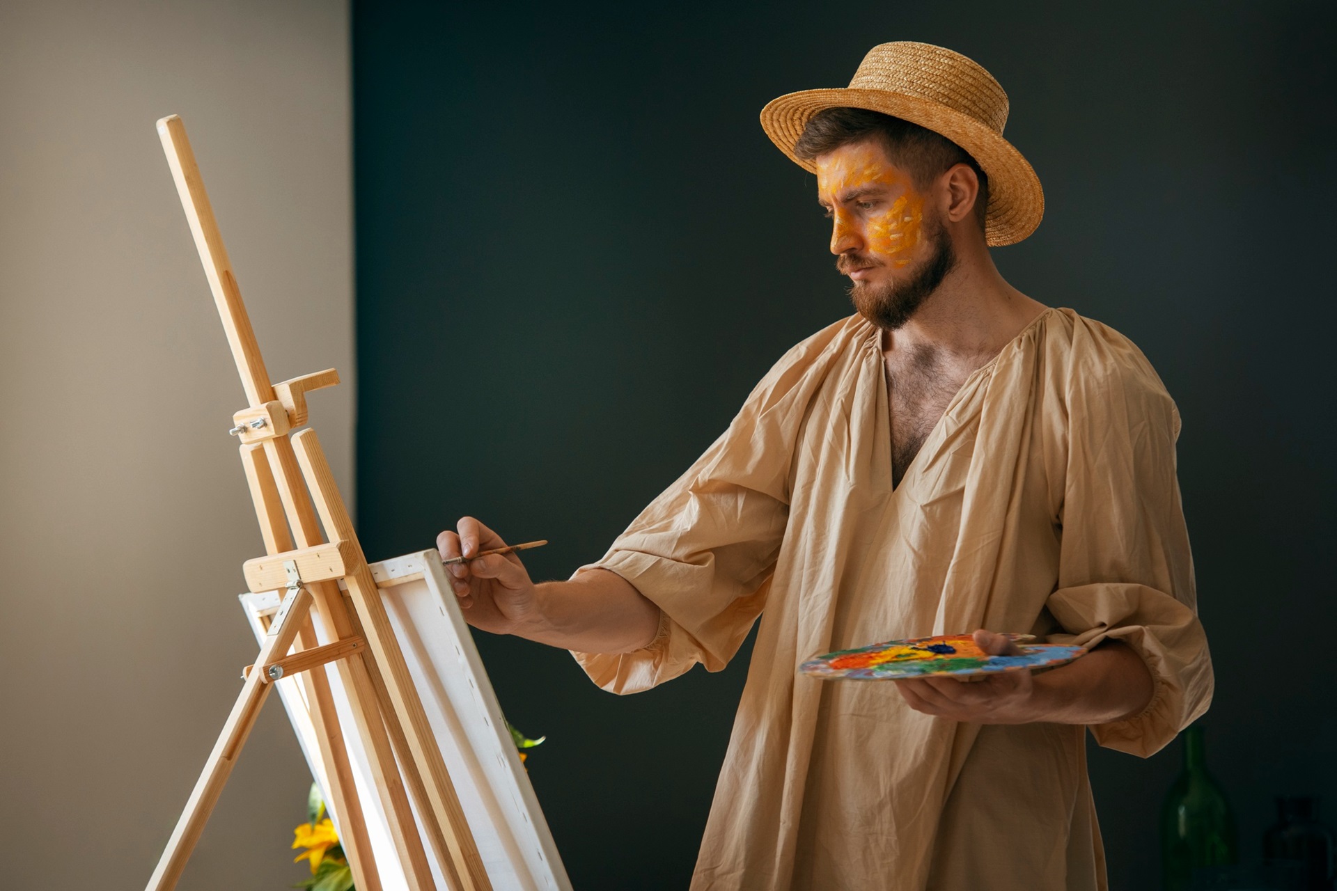 Artista com vestimenta clássica e rosto marcado por tinta amarela pinta sobre tela, segurando uma paleta colorida diante de um cavalete de madeira