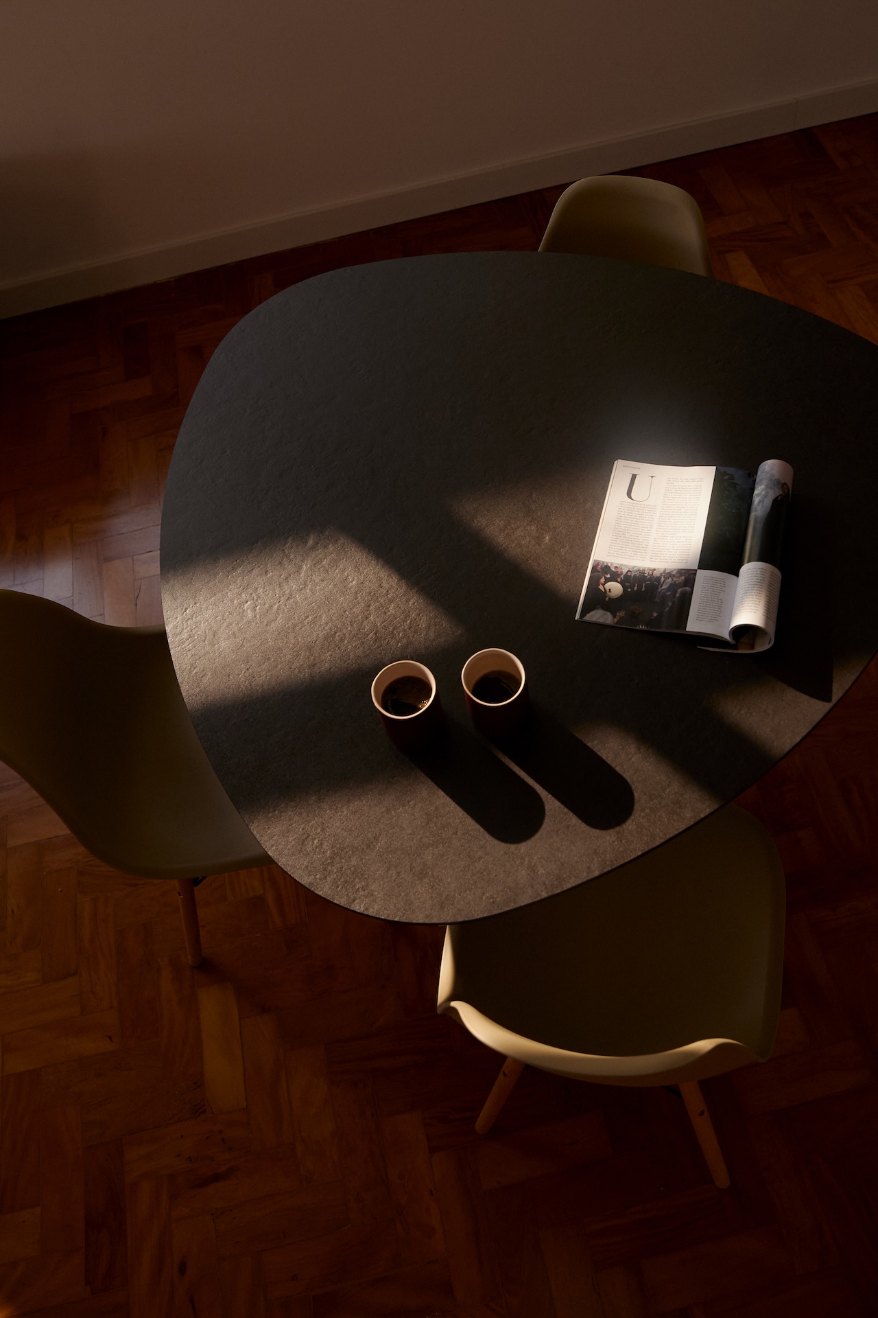 Visão de cima de mesa preta com três cadeiras e piso de taco
