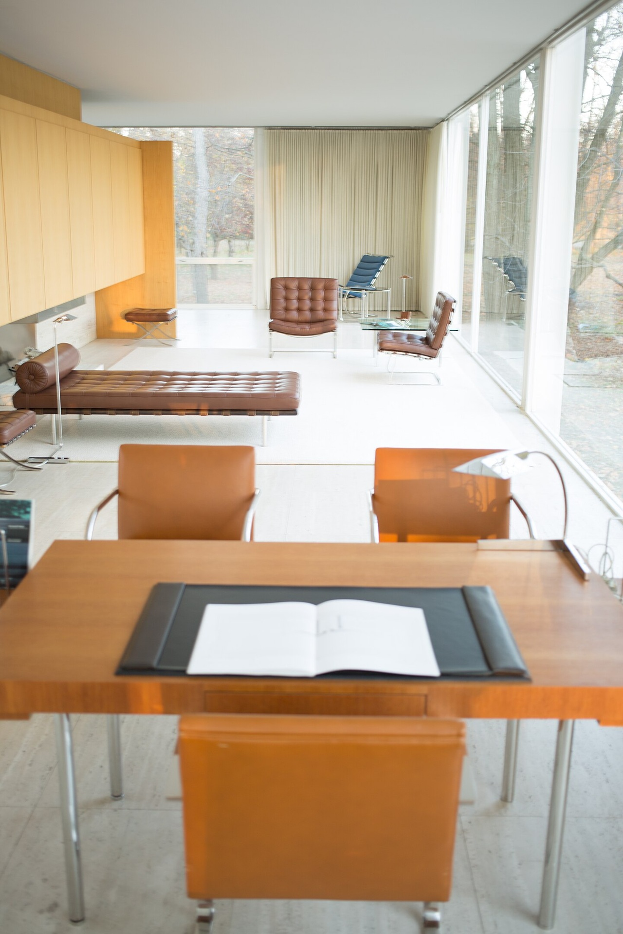 Interior da Farnsworth House com mobiliário projetado por Mies van der Rohe, incluindo poltronas, chaise e mesa de trabalho voltada para as janelas de vidro