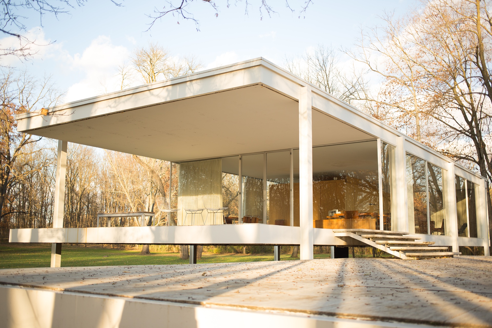 Vista externa da Farnsworth House em dia ensolarado, mostrando a sua estrutura elevada e paredes de vidro, aberta para visitação pública