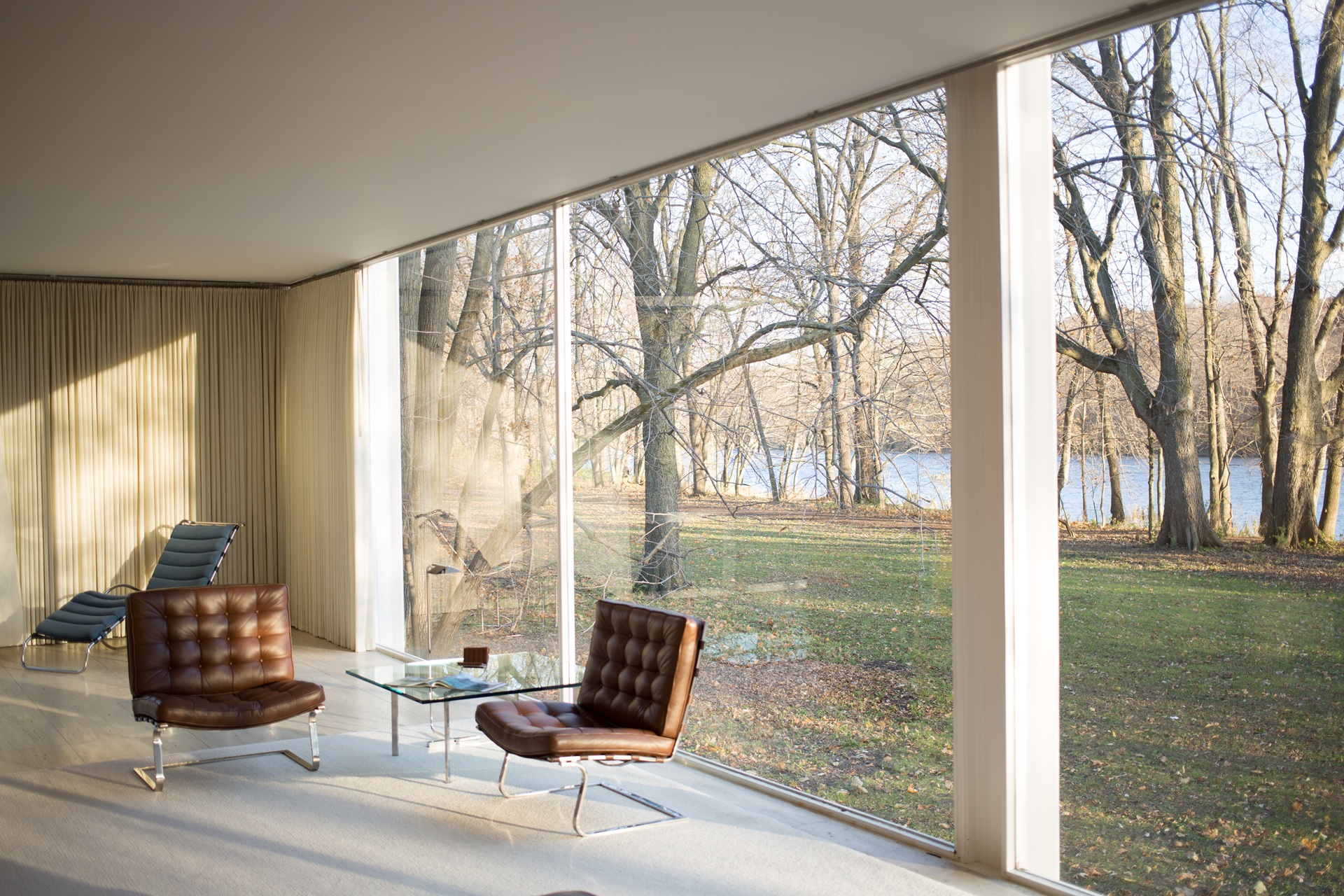 Interior da Farnsworth House com vista para o terreno arborizado e o Rio Fox, patrimônio público aberto à visitação