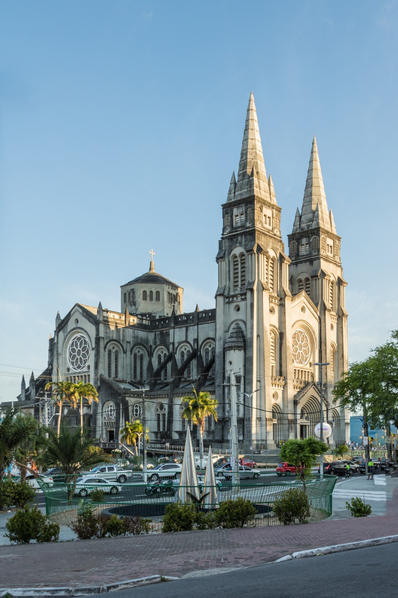 Vista frontal da Catedral Metropolitana de Fortaleza (Catedral de São José): templo monumental em estilo eclético com forte predominância neogótica — duas torres em forma de lanças atingindo aproximadamente 75 m de altura, portada central com arco ogival, grandes vitrais coloridos e fachada em concreto aparente, ocupando parte expressiva da Praça Pedro II