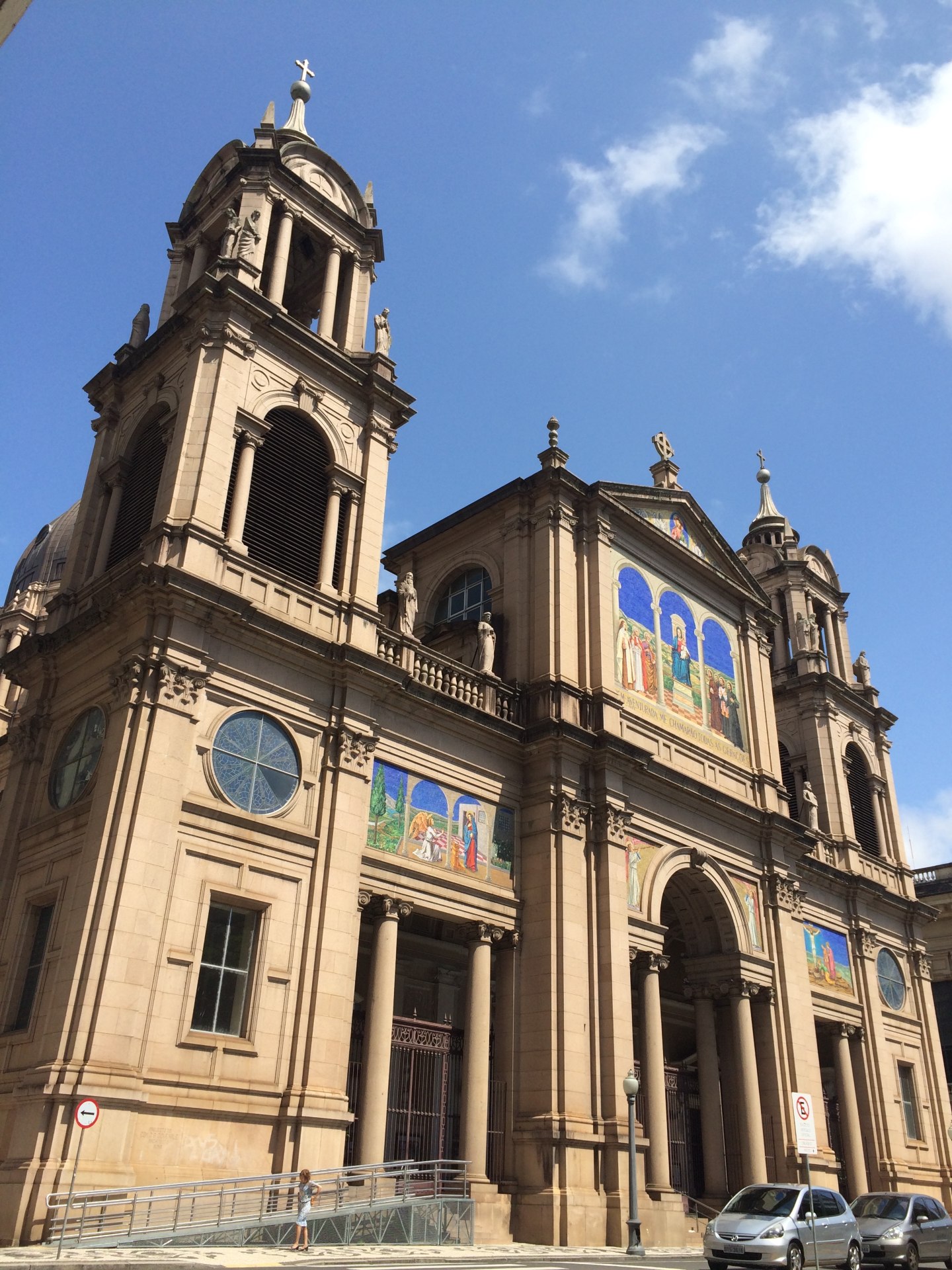 Vista frontal da Catedral Metropolitana de Porto Alegre, destacando sua fachada renascentista com mosaicos coloridos executados pela Academia de Mosaicos do Vaticano. A imponente cúpula e as torres da catedral são visíveis ao fundo, refletindo a grandiosidade da arquitetura religiosa da cidade