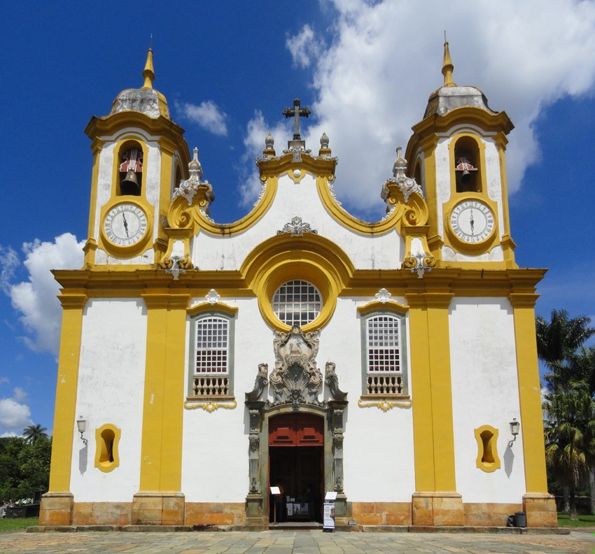 Vista frontal da Igreja Matriz de Santo Antônio, em Tiradentes (MG), destacando sua fachada barroca com esculturas atribuídas a Aleijadinho, incluindo um relógio de sol esculpido em pedra-sabão. O interior é ricamente decorado com talha dourada, altares de estilo rococó e um órgão de tubos português de 1788. A igreja é um ícone da arquitetura colonial brasileira e um símbolo da cidade