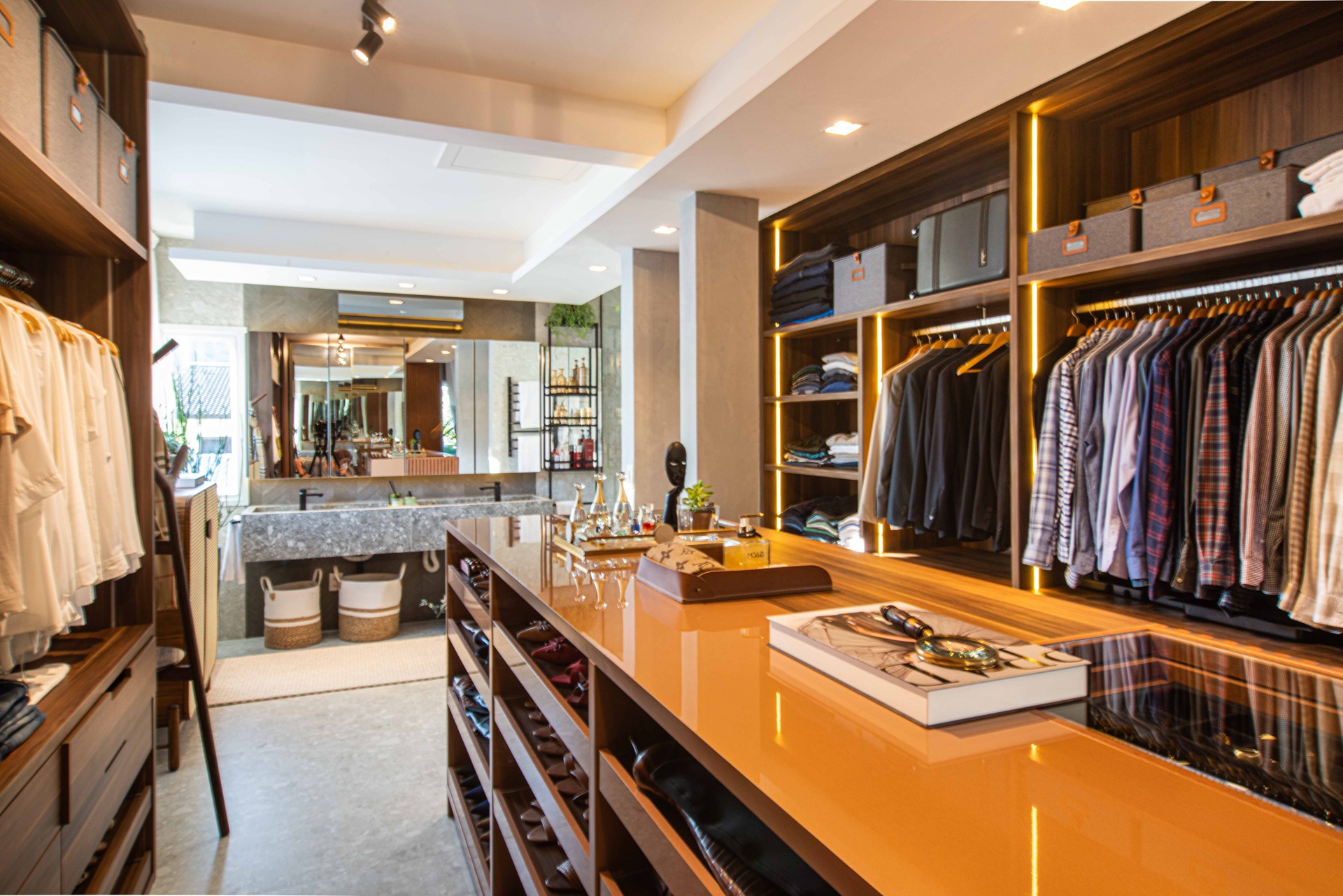 Closet com bancada amadeirada no centro e bancada de banheiro ao fundo