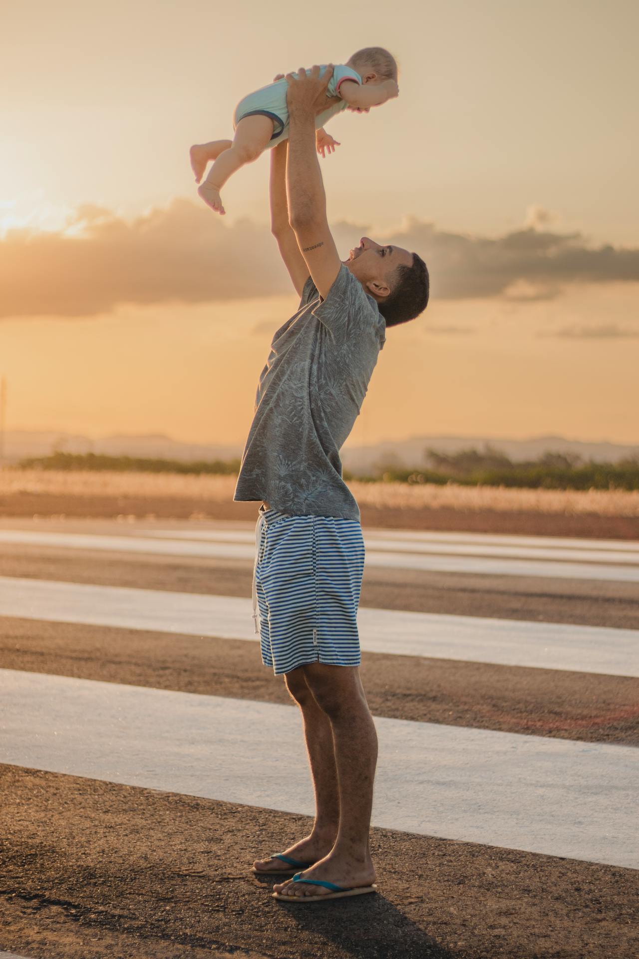 Homem ergue bebê ao pôr do sol, transmitindo leveza, afeto e conexão com o presente