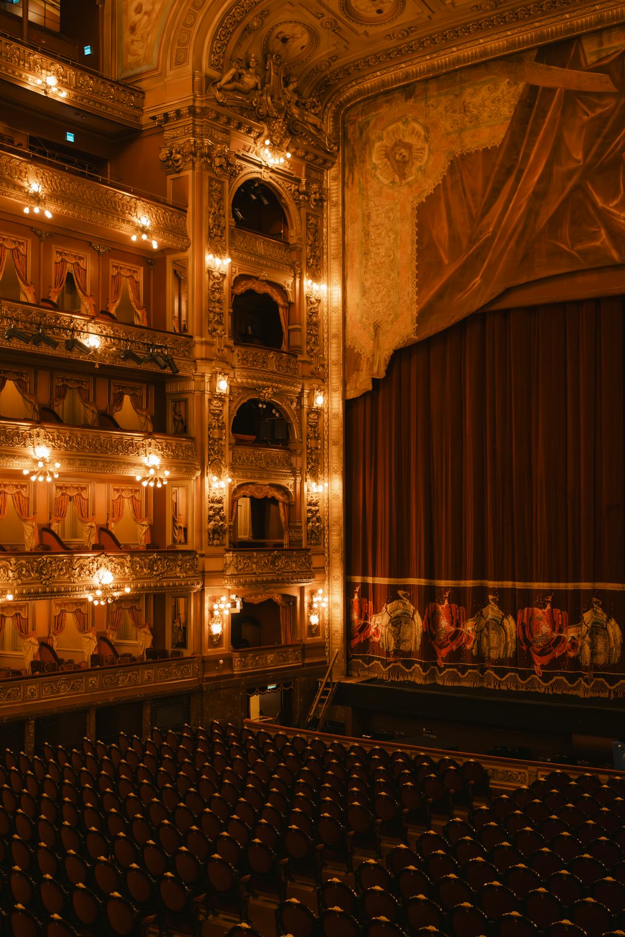 casa de ópera Interior do Teatro Colón, em Buenos Aires, com fileiras de poltronas, camarotes ornamentados com detalhes dourados e cortinas vermelhas, iluminado por luzes quentes que destacam a riqueza arquitetônica do espaço.