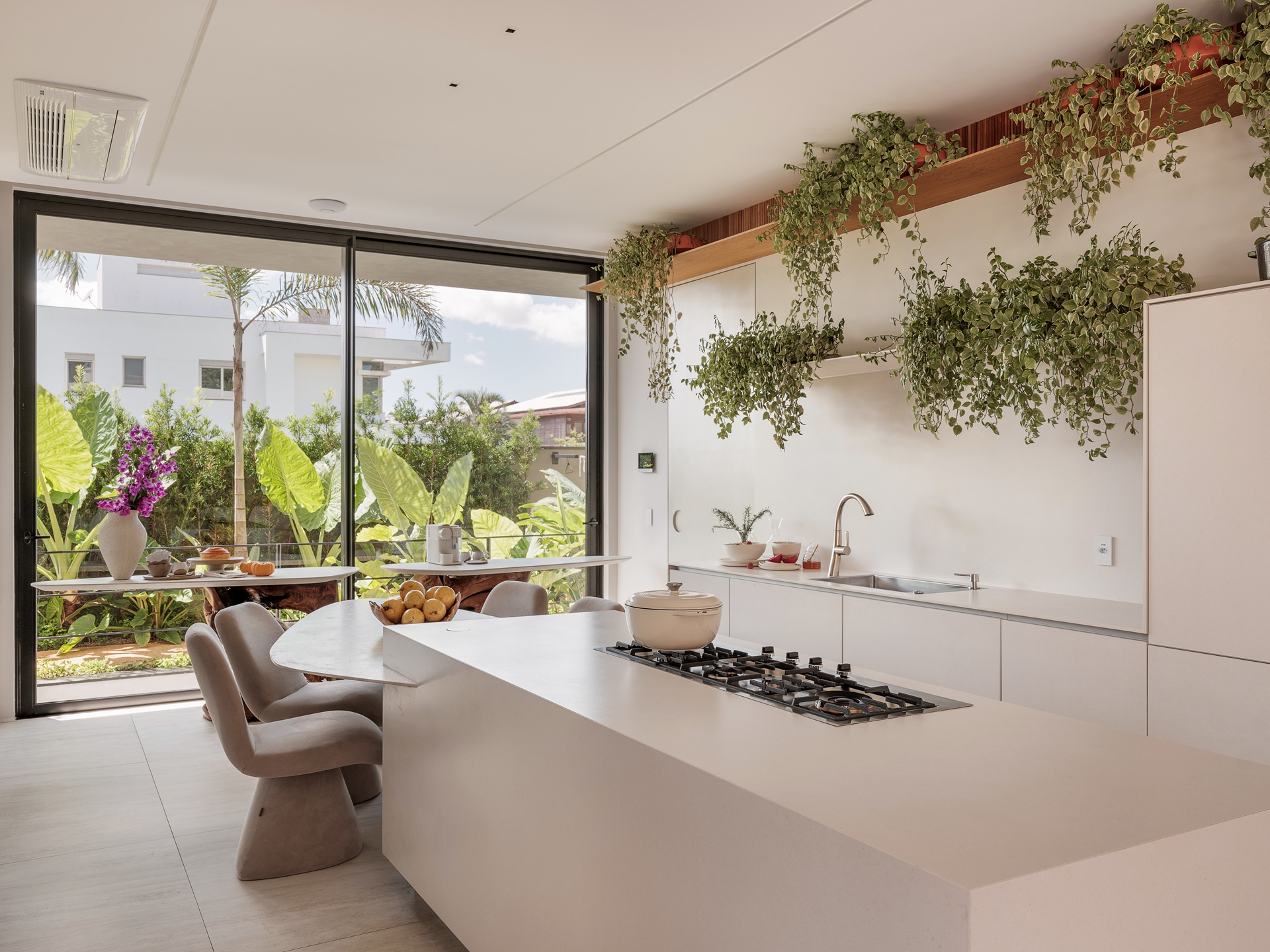 Cozinha em tons claros e neutros com ilha e parede de vidro com vista para paisagismo exterior