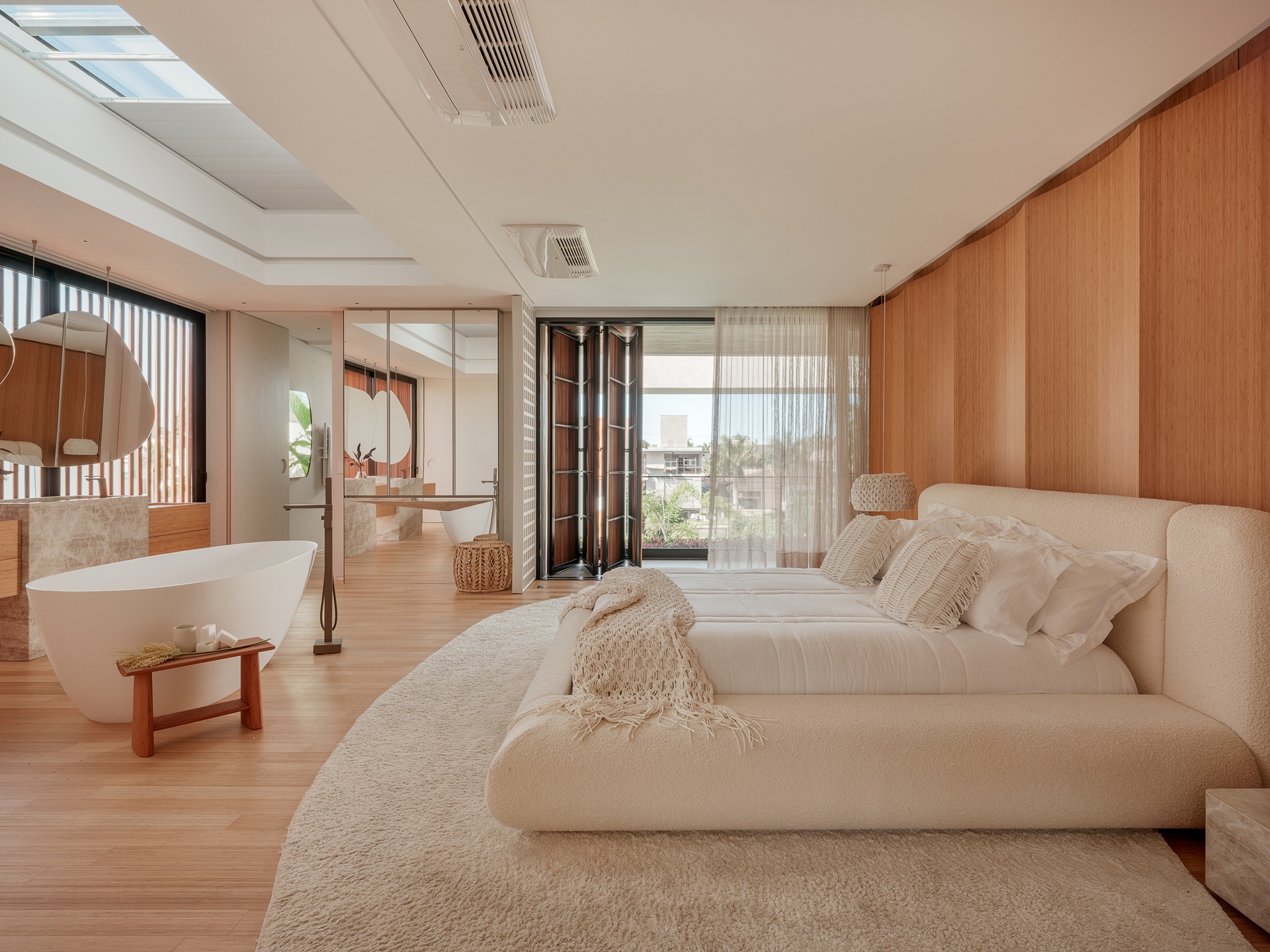 Quarto em tons neutros, com piso e painel de madeira, cama de casal e banheira de imersão