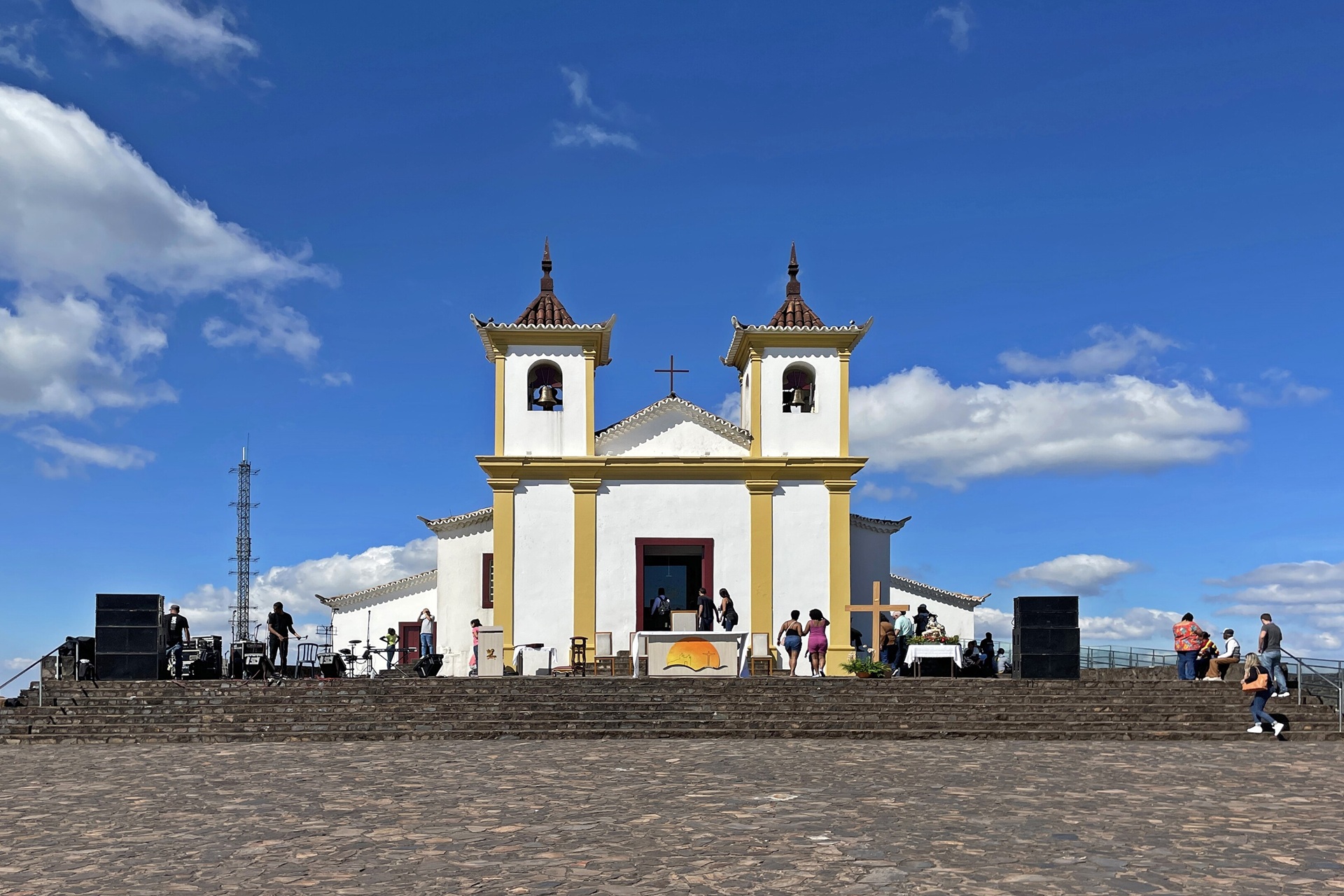 Capela de Nossa Senhora da Piedade em Caeté, Minas Gerais, com fiéis reunidos na escadaria sob céu azul