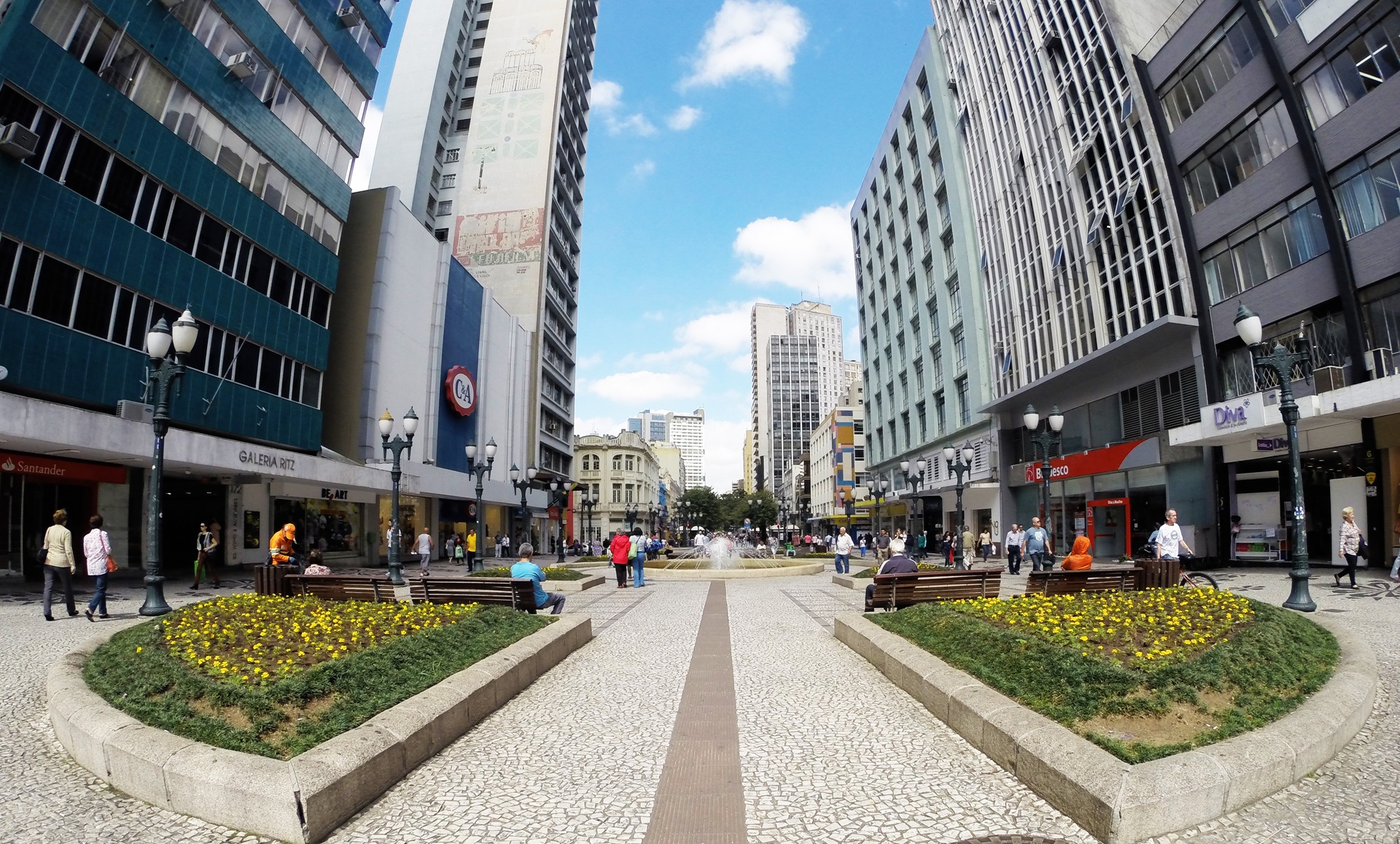 Vista da Rua XV de Novembro, calçadão no centro de Curitiba, com jardins, bancos e prédios ao redor