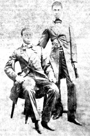 irmaos rebouças Fotografia em preto e branco dos irmãos Rebouças. Um deles está sentado, de terno e gravata, olhando para a câmera com postura firme; o outro está de pé, com a mão apoiada no ombro do irmão, também vestindo paletó e gravata