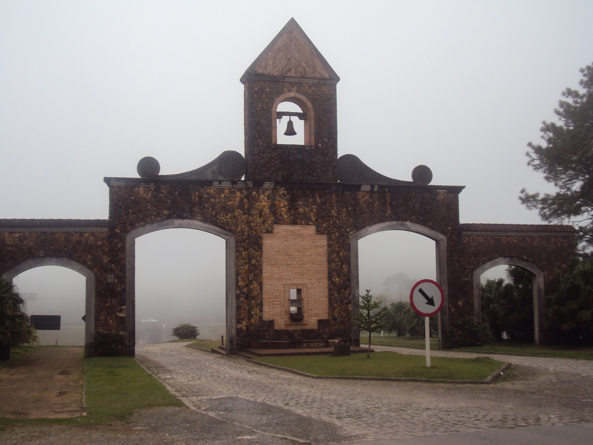 irmaos rebouças Fotografia do pórtico de entrada da Estrada da Graciosa, no Paraná, em um dia de neblina. A estrutura, feita de pedra e tijolo, possui três arcos e uma torre central com sino