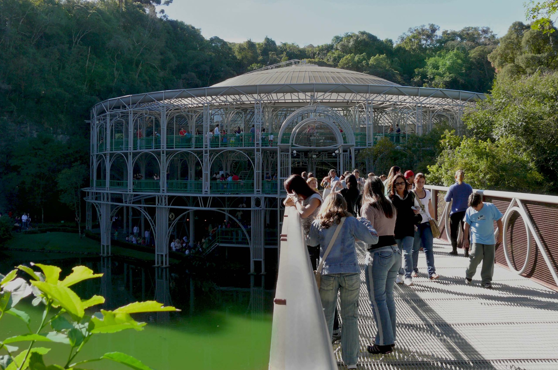 ópera de arame Vista externa da Ópera de Arame com visitantes atravessando a passarela sobre o lago.
