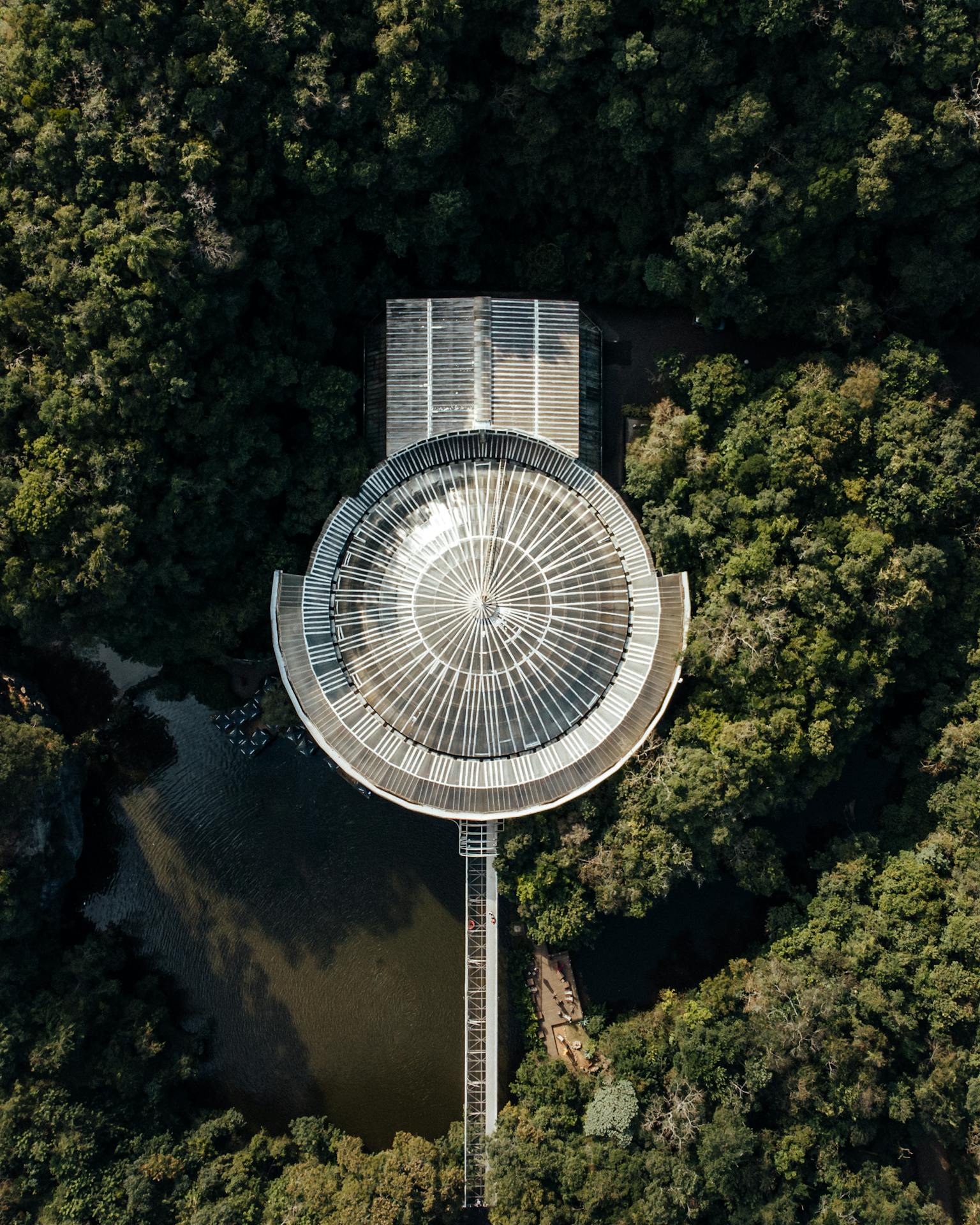 ópera de arame Imagem aérea da Ópera de Arame cercada por vegetação, com lago e passarela central visíveis.
