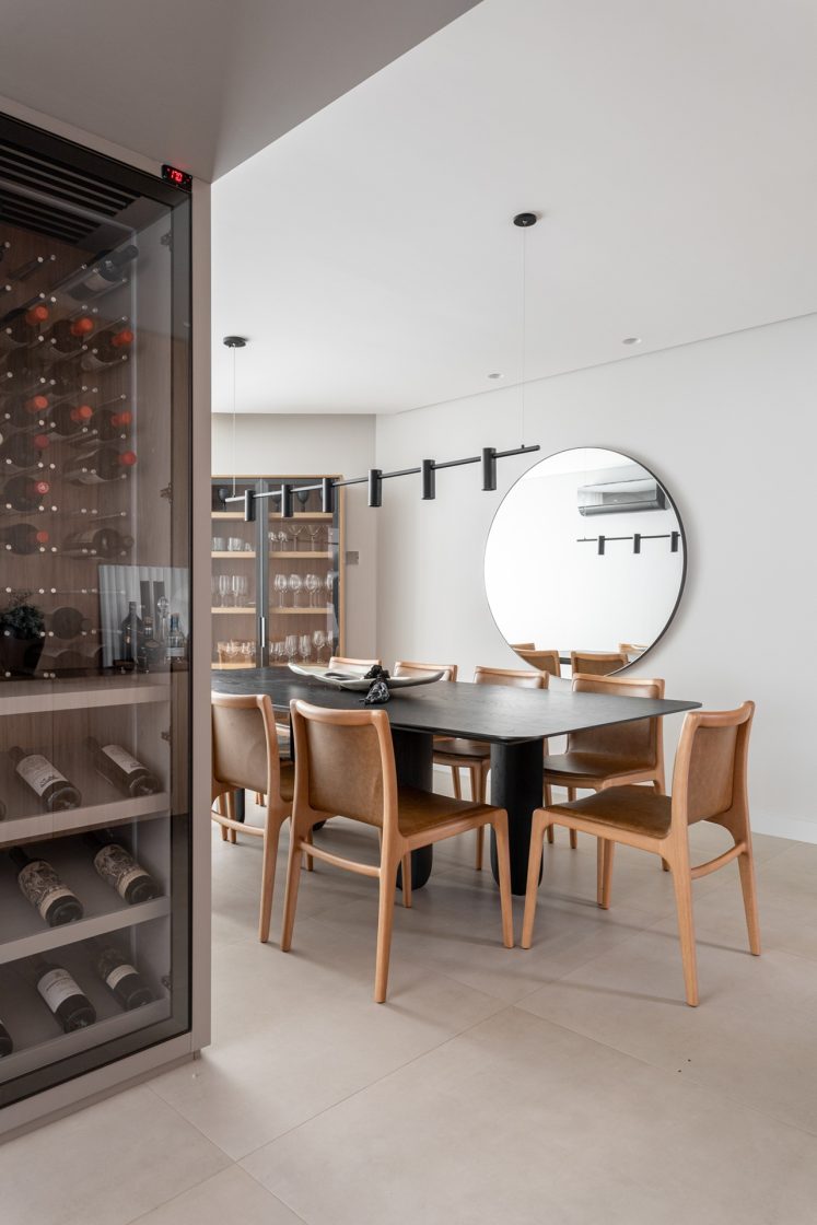 Sala de jantar com mesa preta, cadeiras de madeira e adega para vinhos
