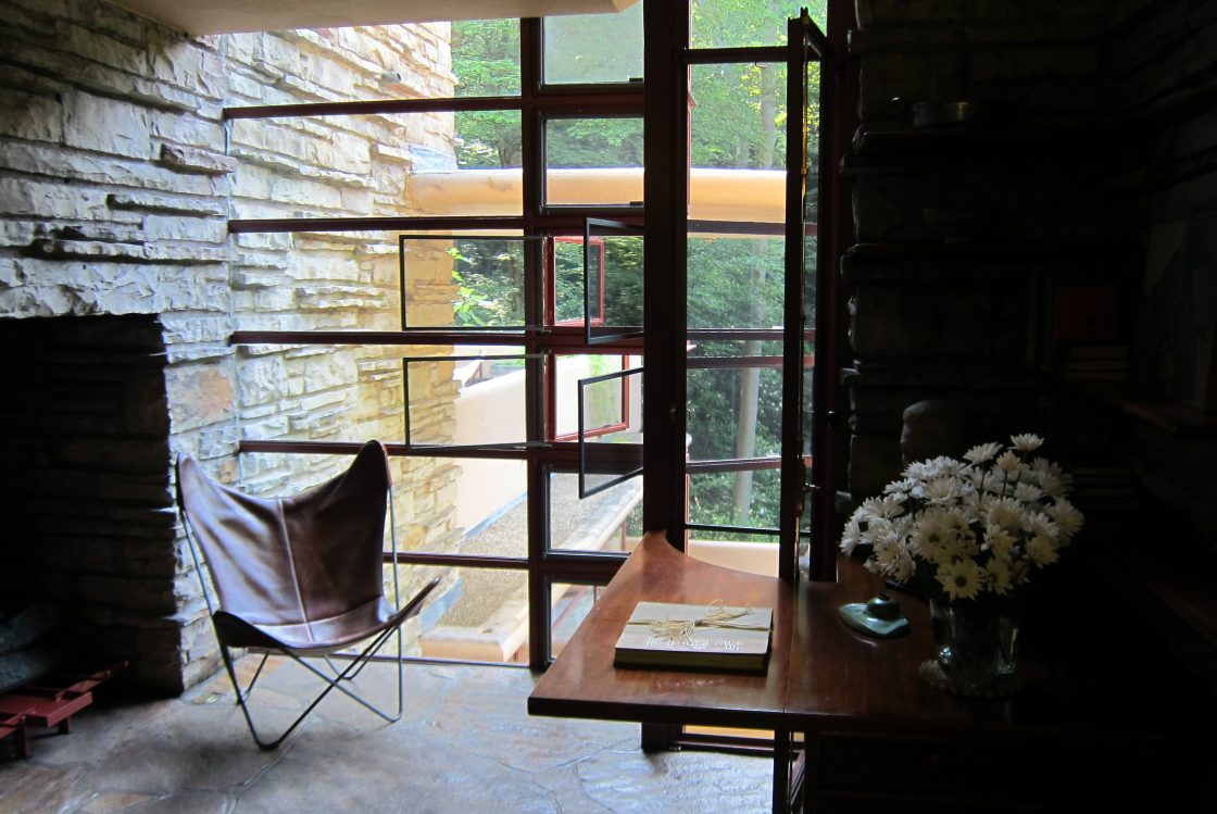 casa da cascata Detalhe de um canto da Fallingwater com lareira, mesa decorada com flores e janelas que se abrem para a paisagem verdejante