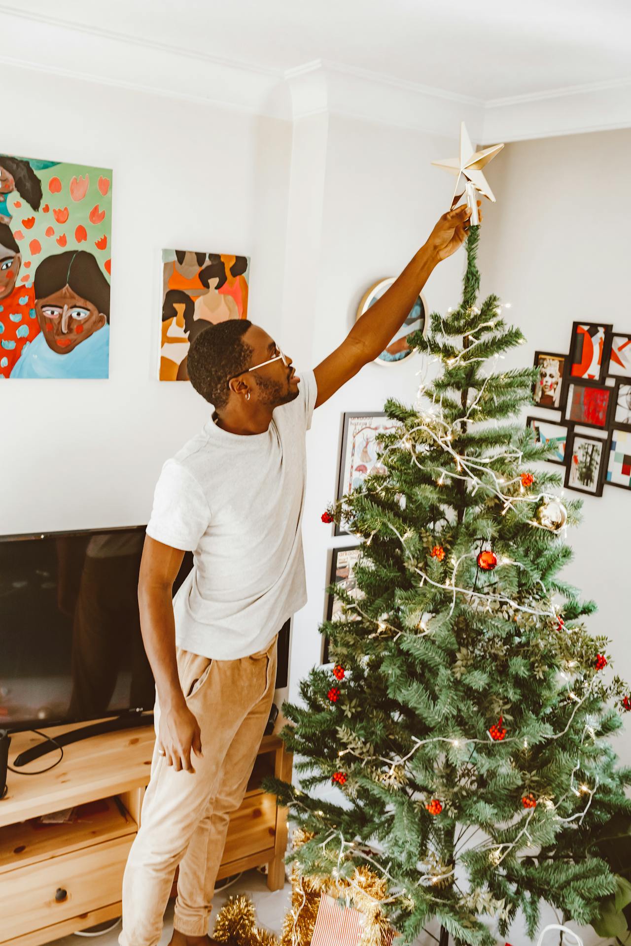 Homem colocando estrela em árvore de Natal em uma sala decorada com quadros
