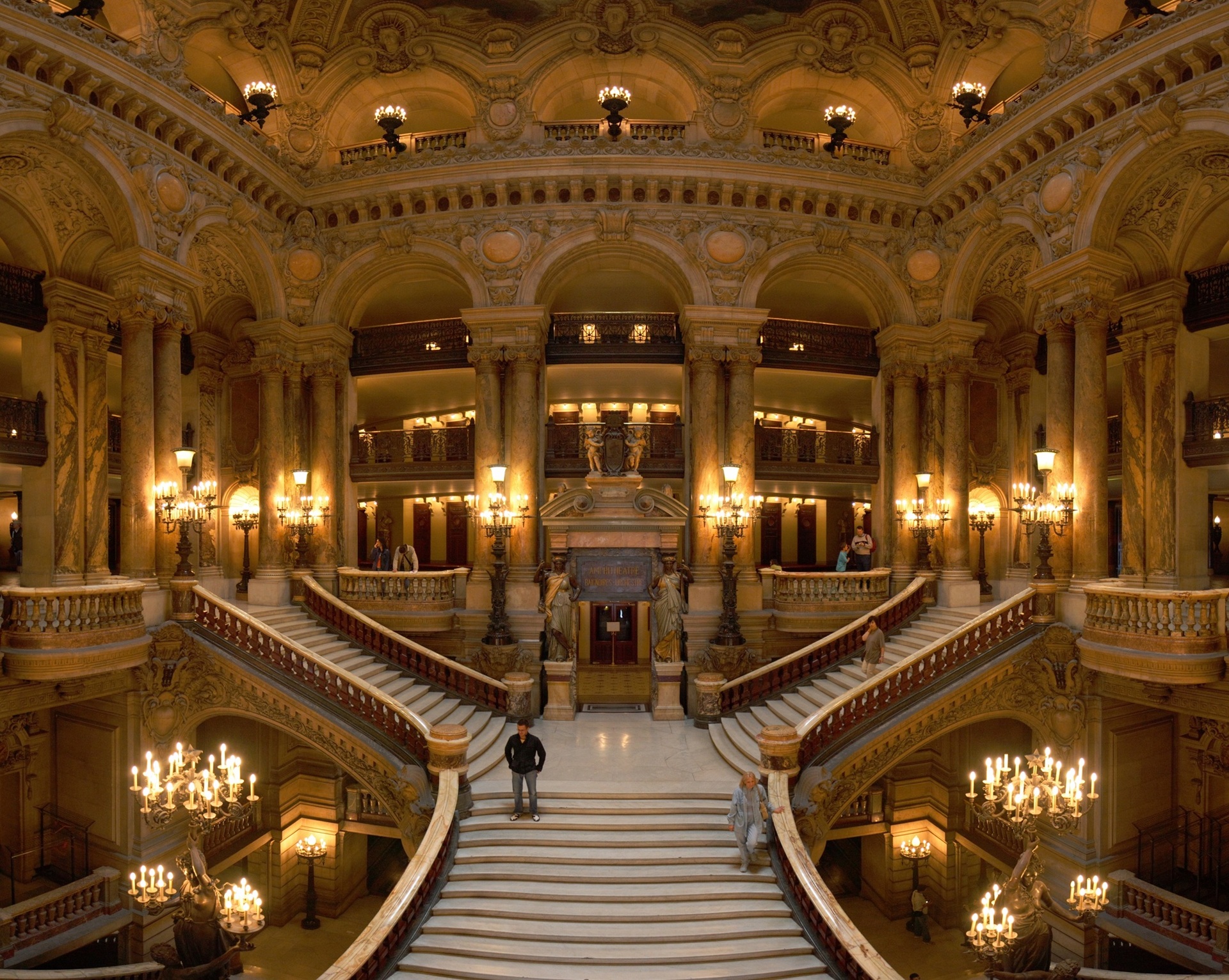 opera garnier Vista ampla do Grand Escalier da Ópera Garnier, em Paris, mostrando a escadaria monumental de mármore branco cercada por colunas douradas, esculturas e candelabros acesos