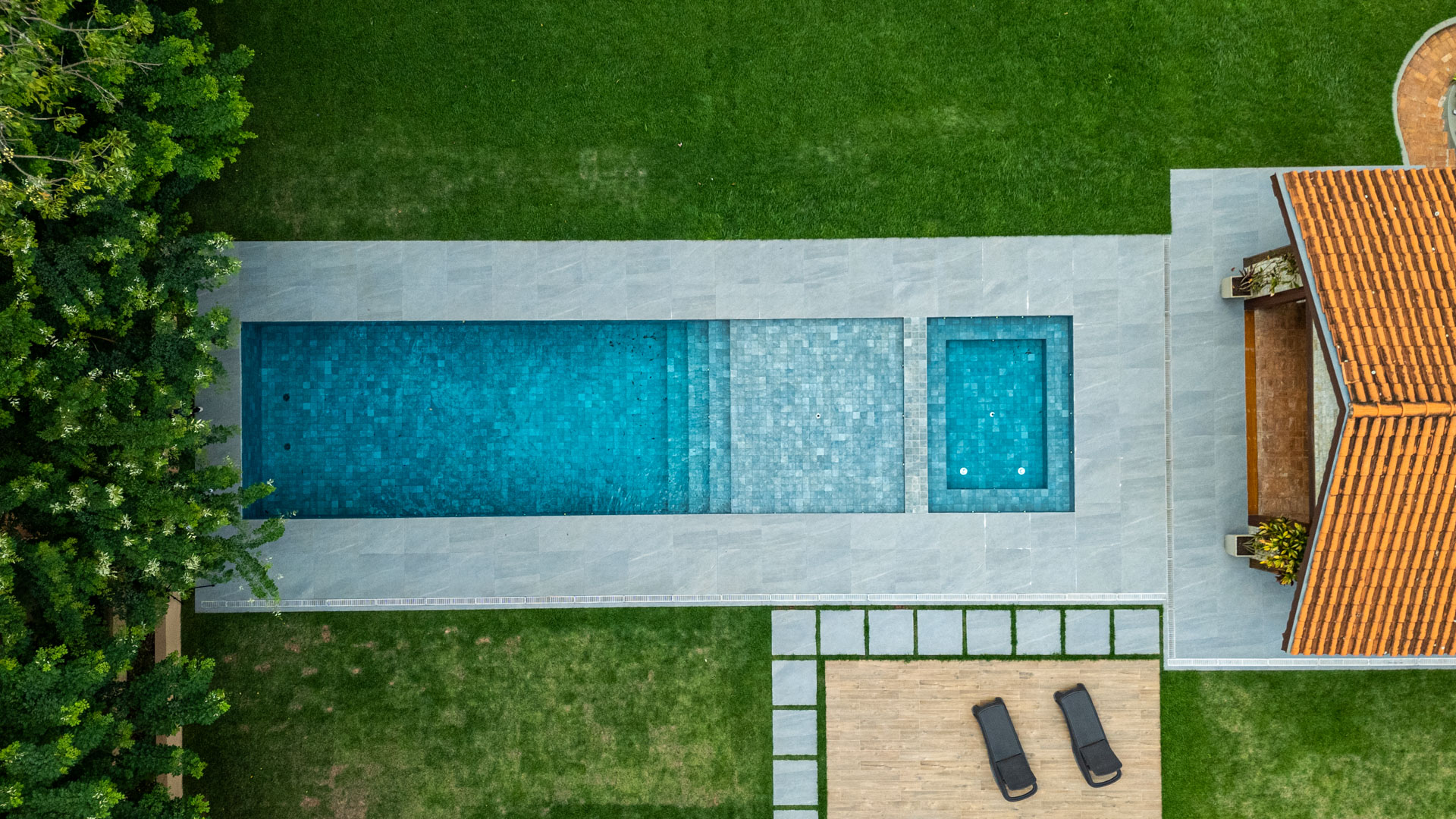 Visão aérea de área externa com piscina de alvenaria azul, pisante em porcelanato e espreguiçadeiras