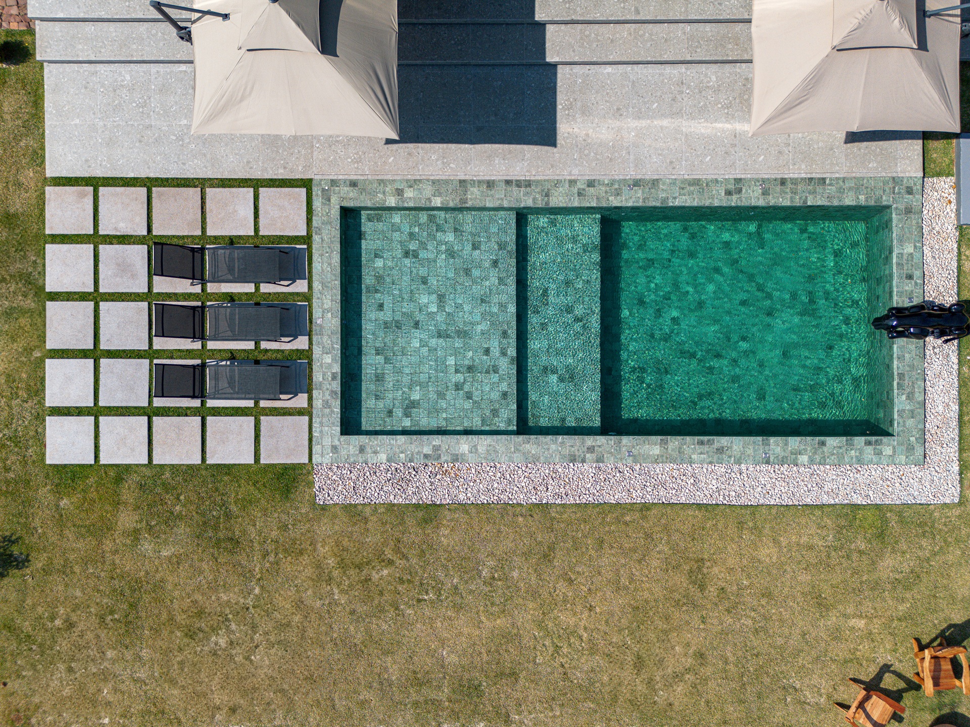 Visão aérea de piscina de alvenaria com pisante para jardim e espreguiçadeiras ao redor