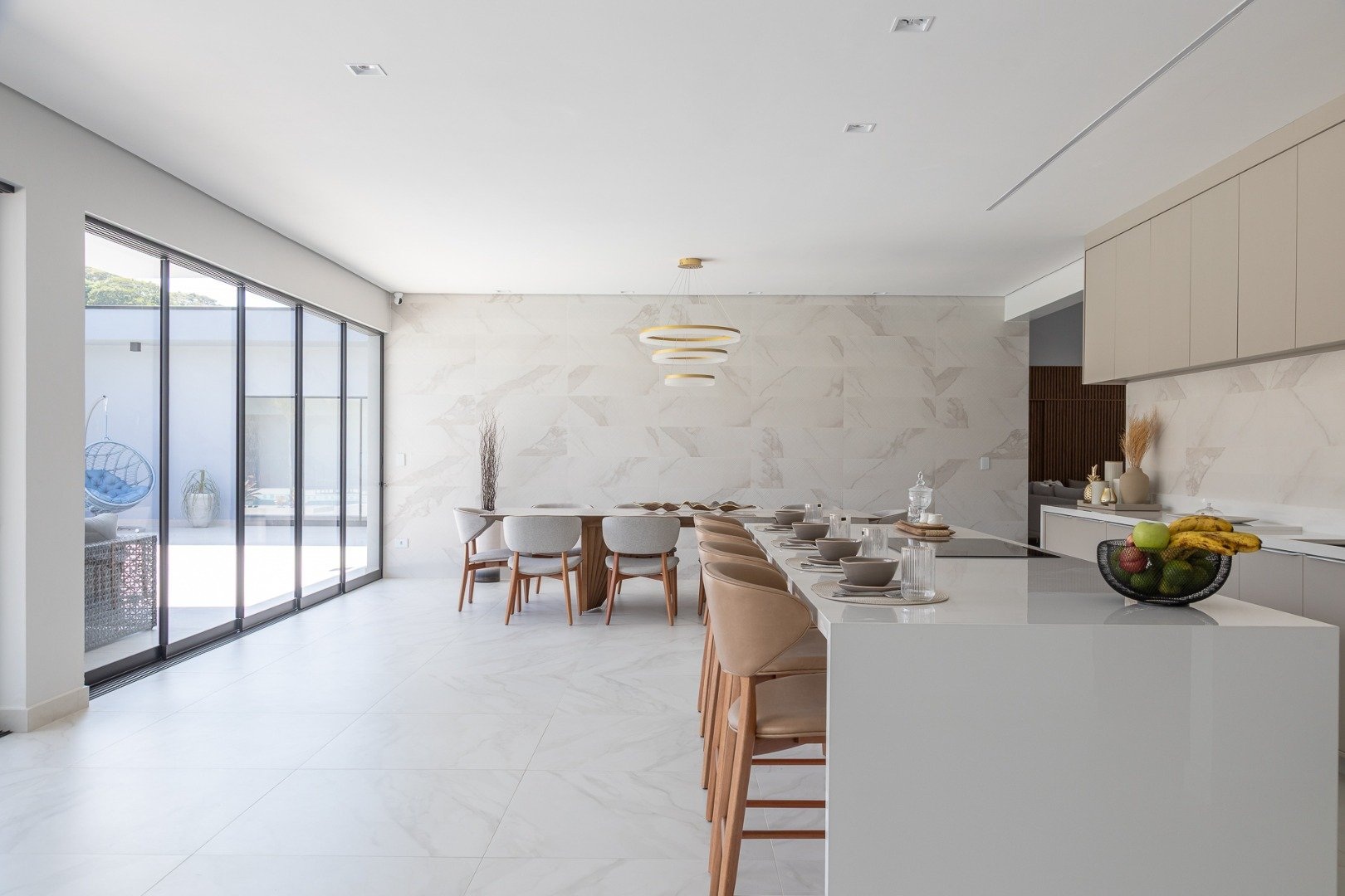 Sala de jantar integrada à cozinha com ilha, ambas com piso que reproduz mármore branco