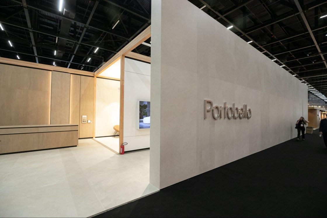 retrospectiva archtrends 2025 Estande da Portobello na Expo Revestir com fachada clean em tons claros, logo metálico aplicado na parede, área interna com painéis amadeirados e iluminação suave, destacando a presença marcante da marca no evento